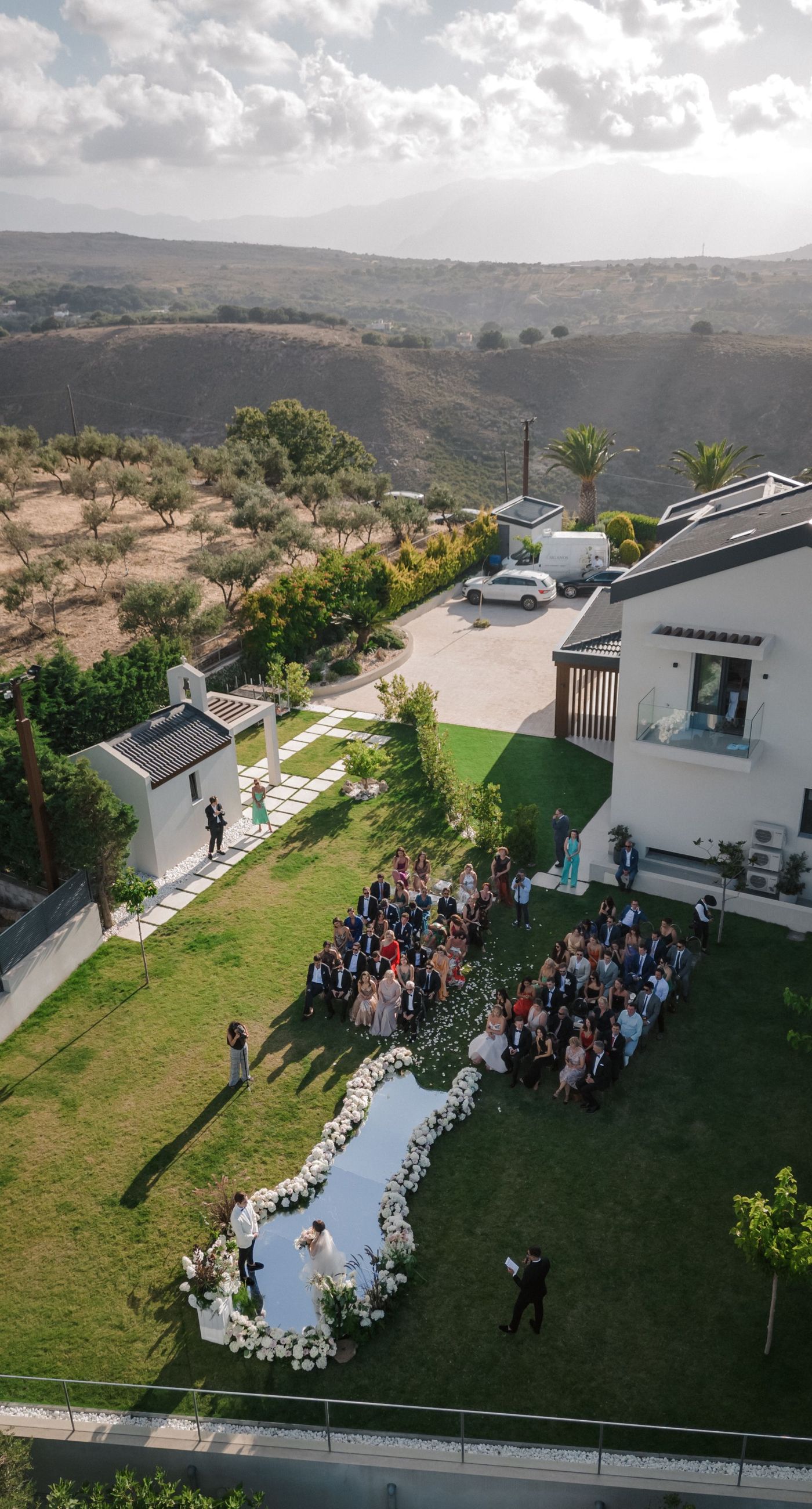  Sasha & Alex - Amidst a breathtaking landscape, this exquisite showcase captures the essence of romance and elegance. Soft hues of blush and ivory blend seamlessly with lush greenery, creating an ethereal garden-like setting. The mirrored aisle reflects the joyful union, adding a touch of glamor to the scene. Delicate florals, thoughtfully arranged, frame the moment, enhancing the dreamy, sophisticated atmosphere. This outdoor celebration perfectly balances natural beauty with refined artistry, embodying the timeless allure of love in a serene, picturesque locale. - Photo 5