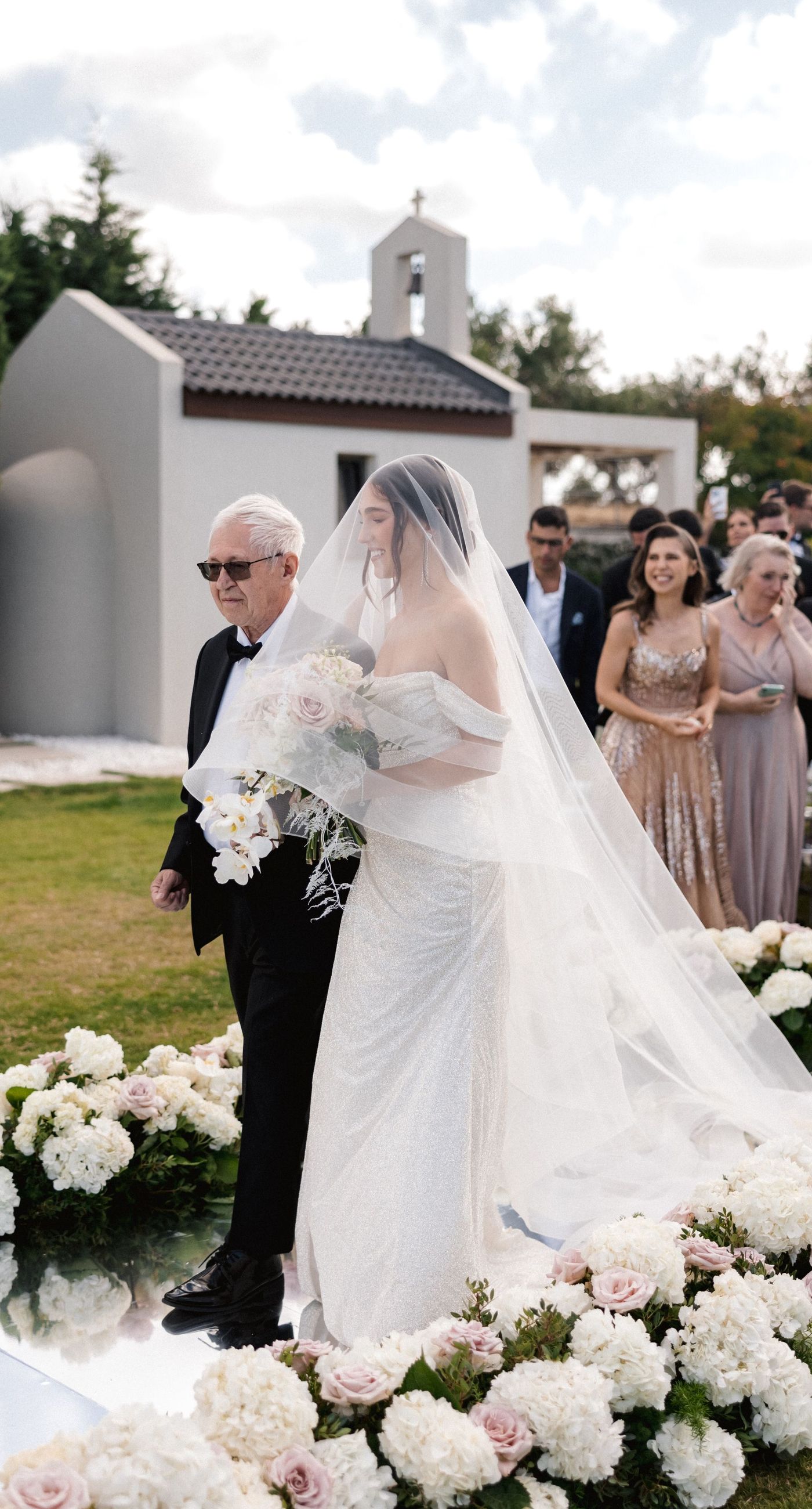  Sasha & Alex - Amidst a breathtaking landscape, this exquisite showcase captures the essence of romance and elegance. Soft hues of blush and ivory blend seamlessly with lush greenery, creating an ethereal garden-like setting. The mirrored aisle reflects the joyful union, adding a touch of glamor to the scene. Delicate florals, thoughtfully arranged, frame the moment, enhancing the dreamy, sophisticated atmosphere. This outdoor celebration perfectly balances natural beauty with refined artistry, embodying the timeless allure of love in a serene, picturesque locale. - Photo 6