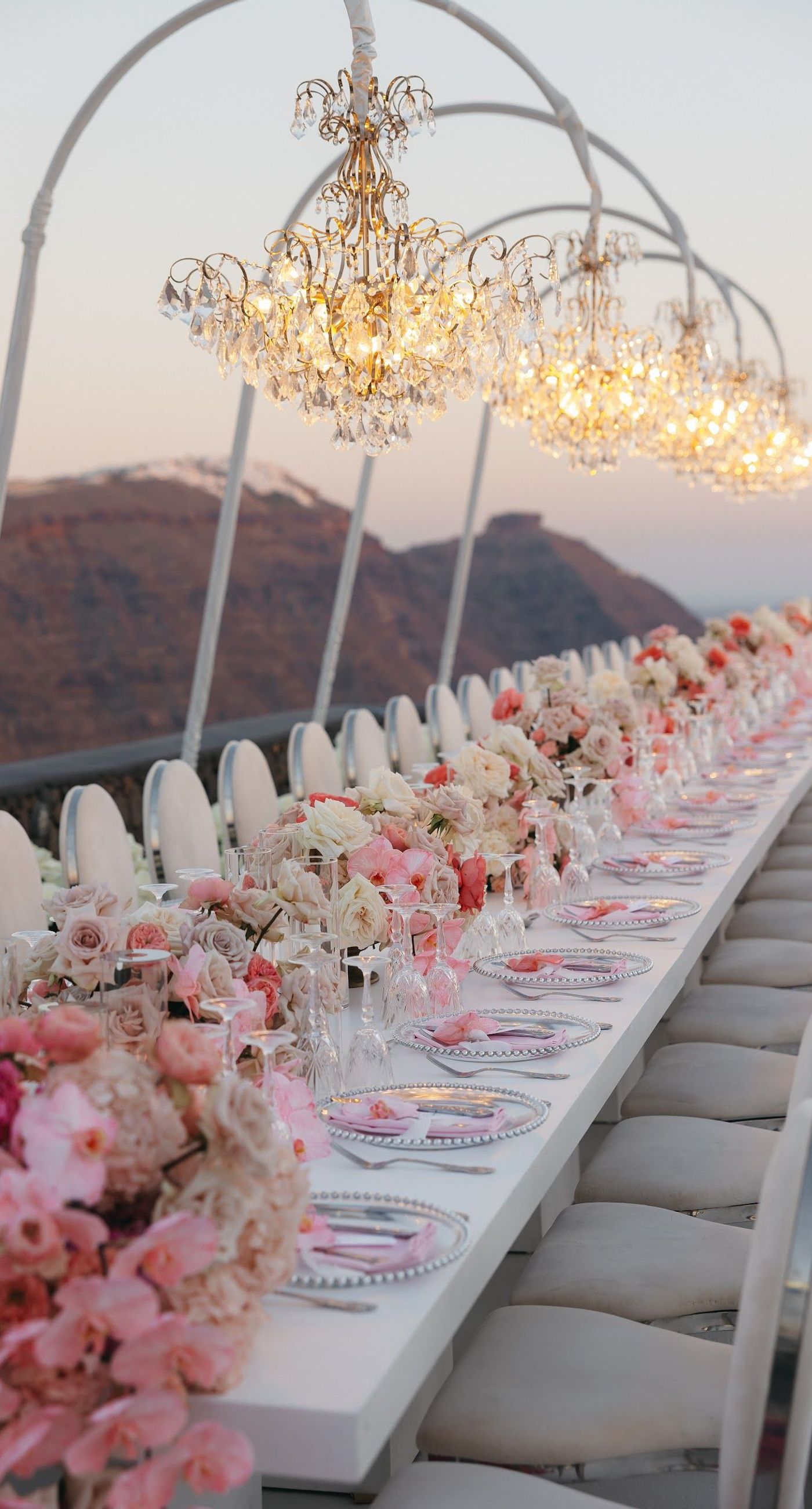 Armita & Azad - A vision of elegance unfolds under a canopy of ethereal blue foliage, accented with white blooms, creating a stunning backdrop for a couple standing in harmonious contrast. Their attire, a dance of monochrome elegance, complements the serene ambiance, while the azure sky and distant cliffs whisper of a hidden paradise. The floor is adorned with cascading white roses, framing the scene with pure grace. The location, with its tranquil vibes and breathtaking views, enhances the overall aesthetic, showcasing a perfect blend of nature and sophistication. This breathtaking display captures the essence of a dreamlike celebration, elevating the floral artistry to new heights. - Photo 6