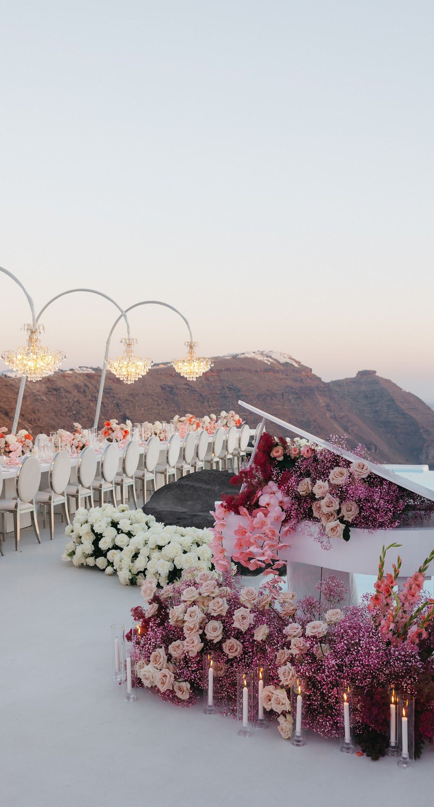 Armita & Azad - A vision of elegance unfolds under a canopy of ethereal blue foliage, accented with white blooms, creating a stunning backdrop for a couple standing in harmonious contrast. Their attire, a dance of monochrome elegance, complements the serene ambiance, while the azure sky and distant cliffs whisper of a hidden paradise. The floor is adorned with cascading white roses, framing the scene with pure grace. The location, with its tranquil vibes and breathtaking views, enhances the overall aesthetic, showcasing a perfect blend of nature and sophistication. This breathtaking display captures the essence of a dreamlike celebration, elevating the floral artistry to new heights. - Photo 8