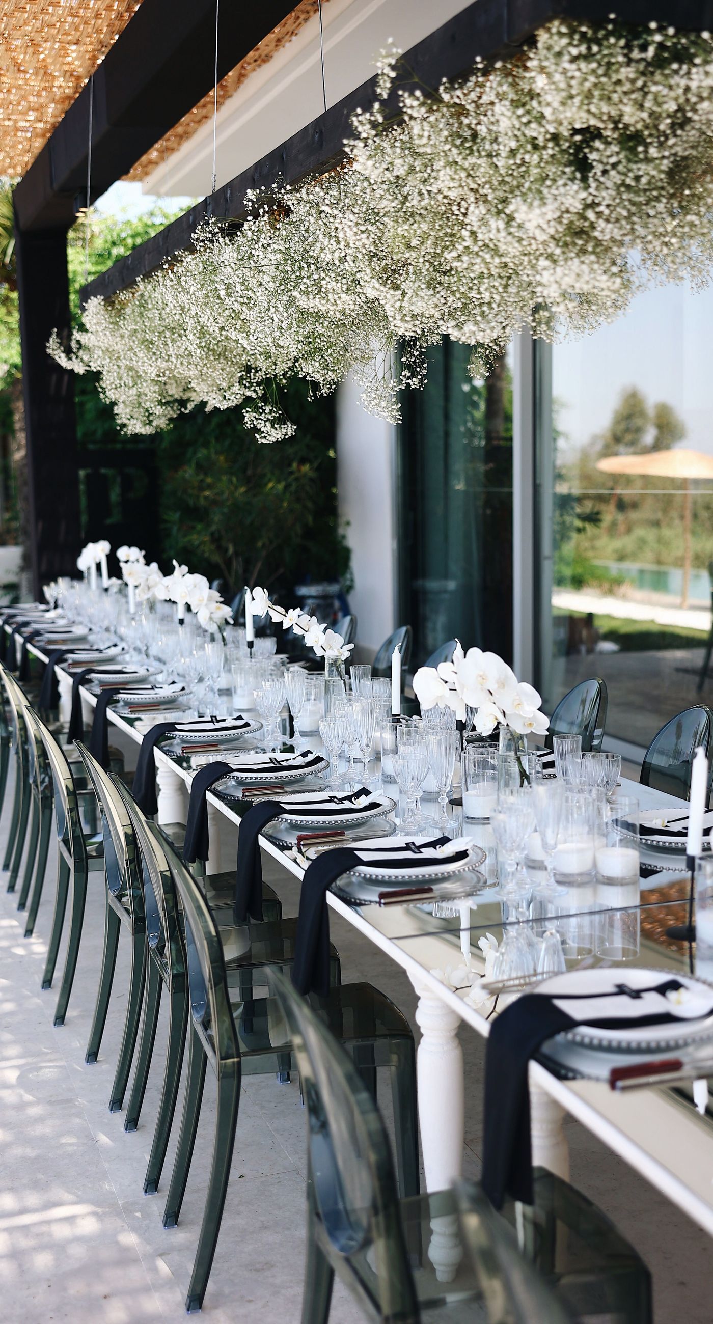 Charlotte & Mateo - In a sunlit scene that marries elegance and joy, a couple strides down an aisle adorned with delicate white petals, while attendees cheerfully shower them with admiration and celebratory petals, embodying a spirit of love and unity. The bride's radiant white gown contrasts beautifully with the subtle greens of the surroundings and the soft blue sky, as the groom's sleek black and white ensemble complements the sophisticated atmosphere. Lush greenery and a graceful arch laced with florals set an enchanting stage, making this moment an exquisite testimony to a florist's craft, capturing both the grandeur and warmth of the occasion. - Photo 7