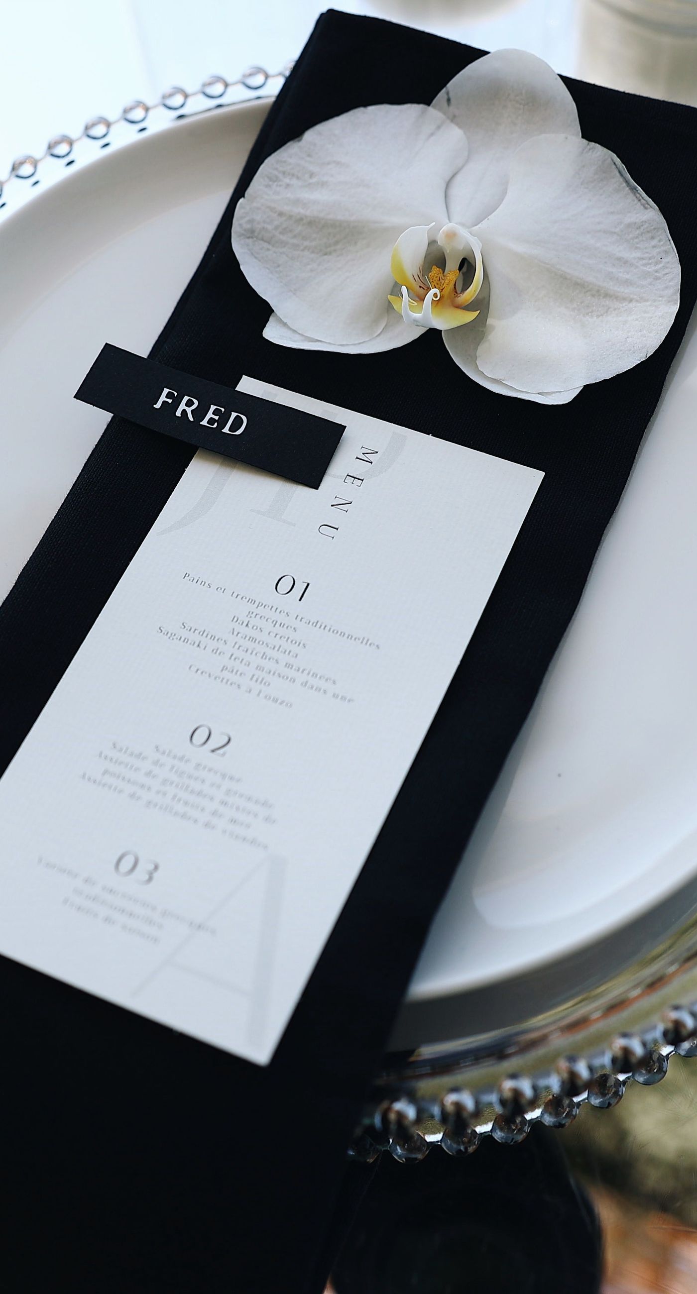 Charlotte & Mateo - In a sunlit scene that marries elegance and joy, a couple strides down an aisle adorned with delicate white petals, while attendees cheerfully shower them with admiration and celebratory petals, embodying a spirit of love and unity. The bride's radiant white gown contrasts beautifully with the subtle greens of the surroundings and the soft blue sky, as the groom's sleek black and white ensemble complements the sophisticated atmosphere. Lush greenery and a graceful arch laced with florals set an enchanting stage, making this moment an exquisite testimony to a florist's craft, capturing both the grandeur and warmth of the occasion. - Photo 9