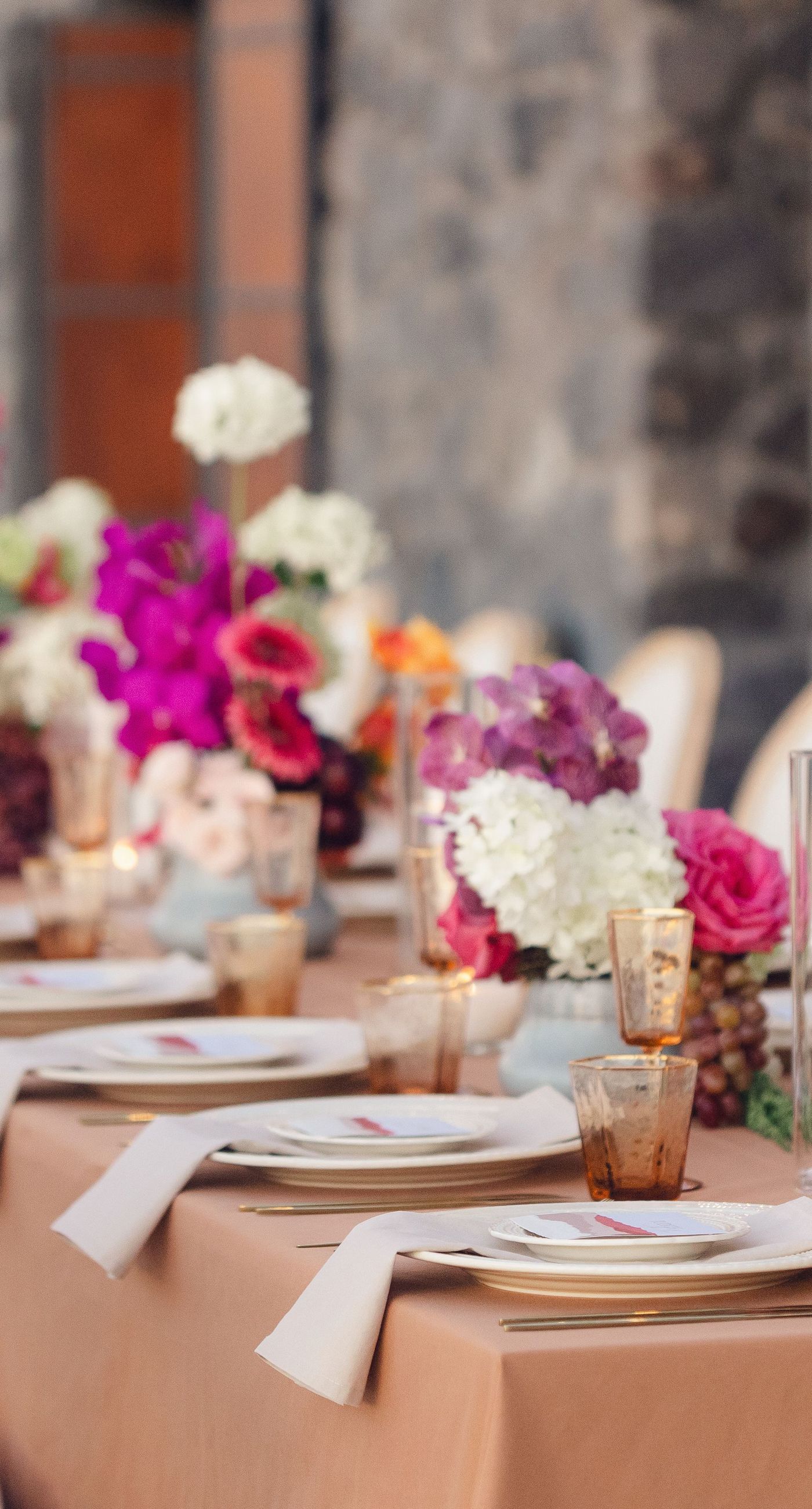 Chris & Jazmin - In a dreamlike setting beneath the soft embrace of the sun, this captivating work embodies a perfect union of elegance and romance. The delicate lace of her gown interlaces with the tender embrace of her partner, creating an ethereal atmosphere amidst the tranquil architecture. A vibrant bouquet bursts with life, featuring an exquisite medley of fuchsia, orange, and deep crimson blooms, each petal whispering tales of timeless love. The muted tones of the setting contrast beautifully with the vivid flowers, offering a glimpse into a serene world where artistry and nature harmonize flawlessly. This presentation speaks to the profound beauty that can blossom in moments of connection. - Photo 10