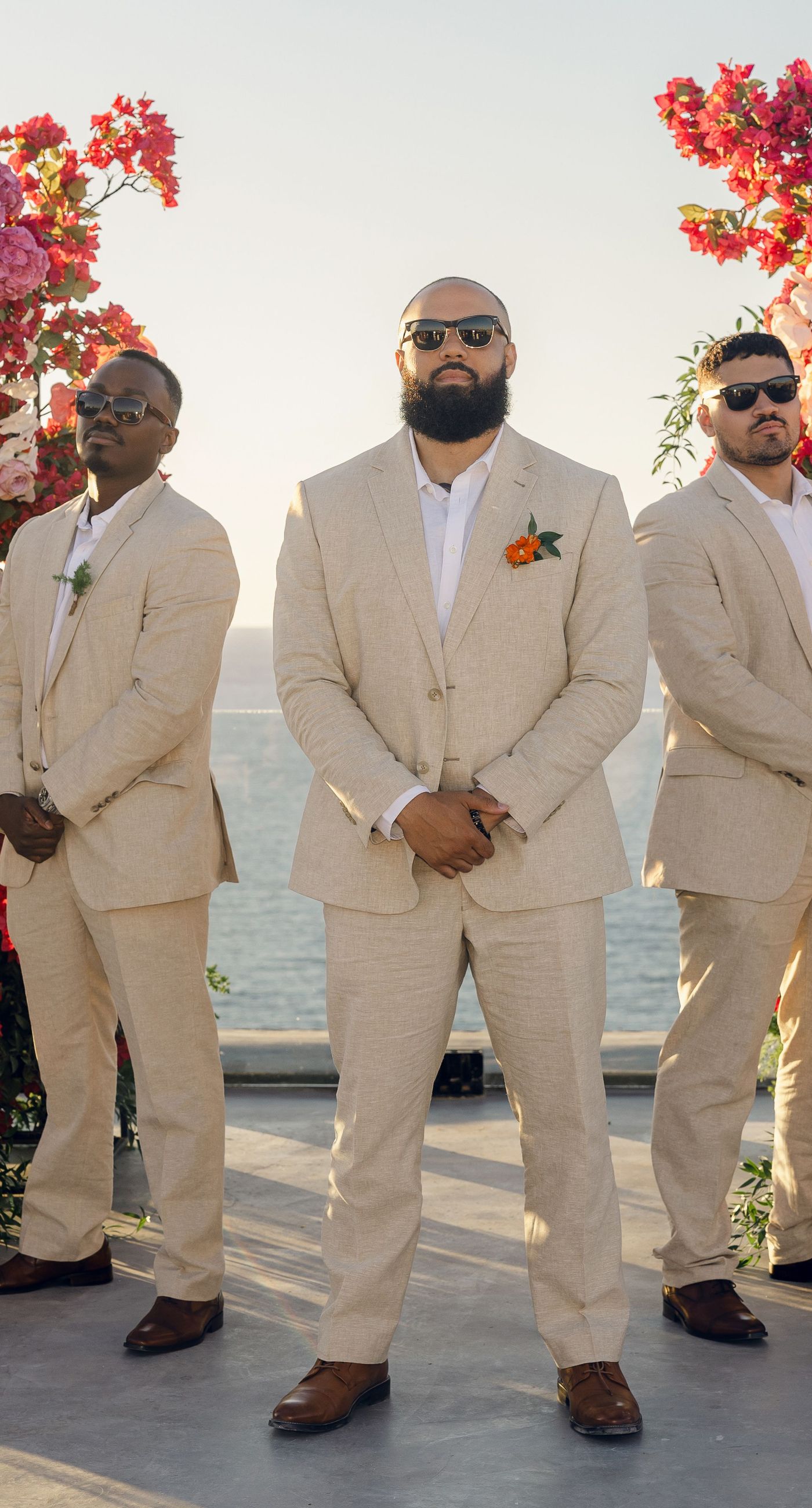 Chris & Jazmin - In a dreamlike setting beneath the soft embrace of the sun, this captivating work embodies a perfect union of elegance and romance. The delicate lace of her gown interlaces with the tender embrace of her partner, creating an ethereal atmosphere amidst the tranquil architecture. A vibrant bouquet bursts with life, featuring an exquisite medley of fuchsia, orange, and deep crimson blooms, each petal whispering tales of timeless love. The muted tones of the setting contrast beautifully with the vivid flowers, offering a glimpse into a serene world where artistry and nature harmonize flawlessly. This presentation speaks to the profound beauty that can blossom in moments of connection. - Photo 5