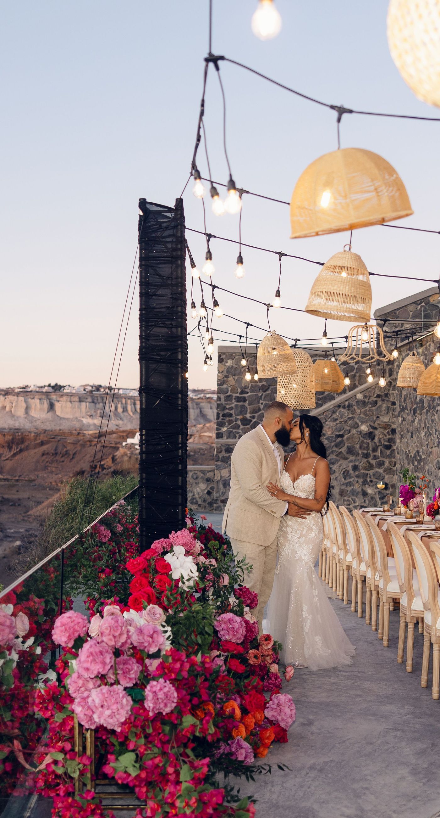 Chris & Jazmin - In a dreamlike setting beneath the soft embrace of the sun, this captivating work embodies a perfect union of elegance and romance. The delicate lace of her gown interlaces with the tender embrace of her partner, creating an ethereal atmosphere amidst the tranquil architecture. A vibrant bouquet bursts with life, featuring an exquisite medley of fuchsia, orange, and deep crimson blooms, each petal whispering tales of timeless love. The muted tones of the setting contrast beautifully with the vivid flowers, offering a glimpse into a serene world where artistry and nature harmonize flawlessly. This presentation speaks to the profound beauty that can blossom in moments of connection. - Photo 6