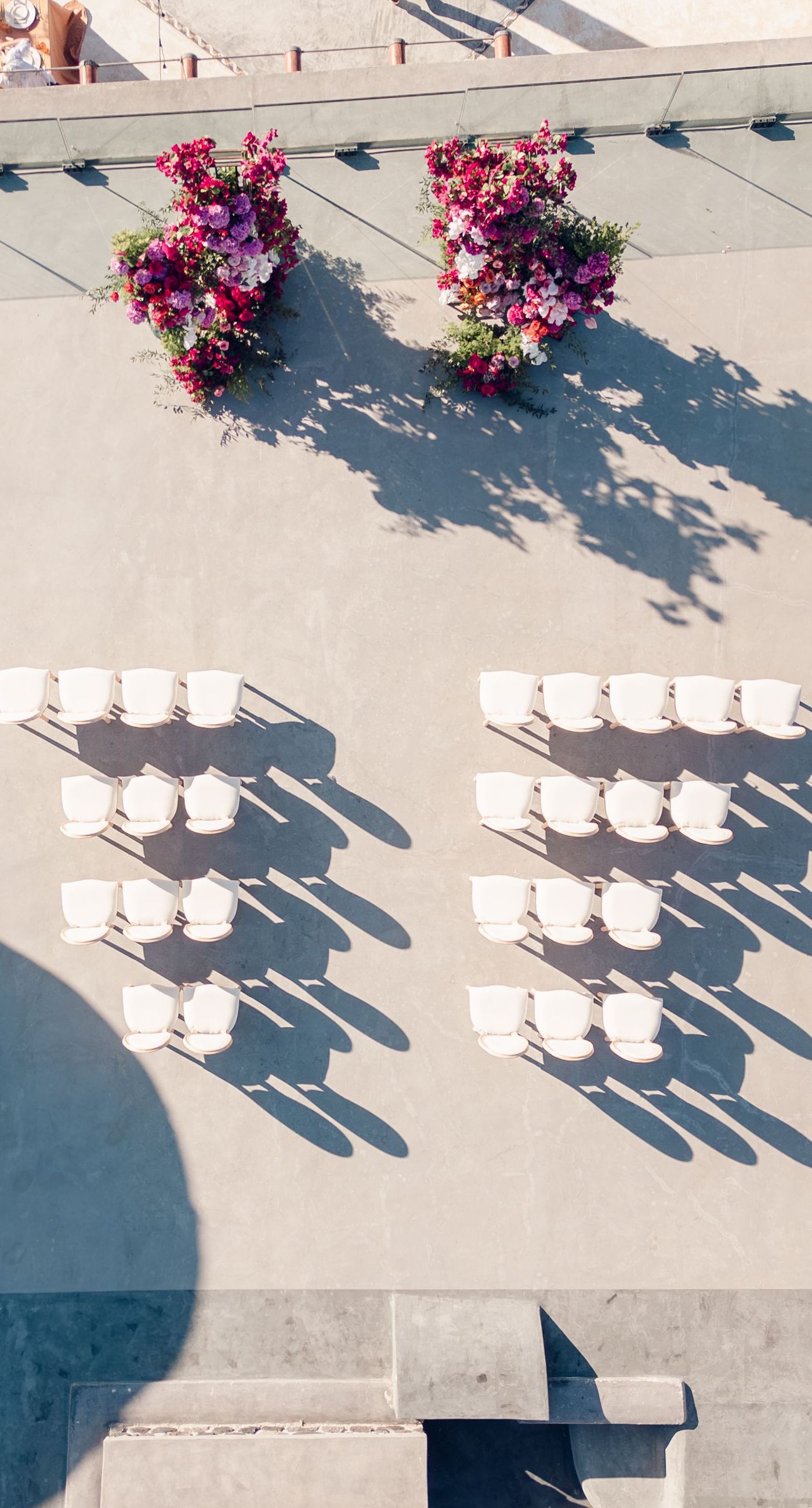 Chris & Jazmin - In a dreamlike setting beneath the soft embrace of the sun, this captivating work embodies a perfect union of elegance and romance. The delicate lace of her gown interlaces with the tender embrace of her partner, creating an ethereal atmosphere amidst the tranquil architecture. A vibrant bouquet bursts with life, featuring an exquisite medley of fuchsia, orange, and deep crimson blooms, each petal whispering tales of timeless love. The muted tones of the setting contrast beautifully with the vivid flowers, offering a glimpse into a serene world where artistry and nature harmonize flawlessly. This presentation speaks to the profound beauty that can blossom in moments of connection. - Photo 1