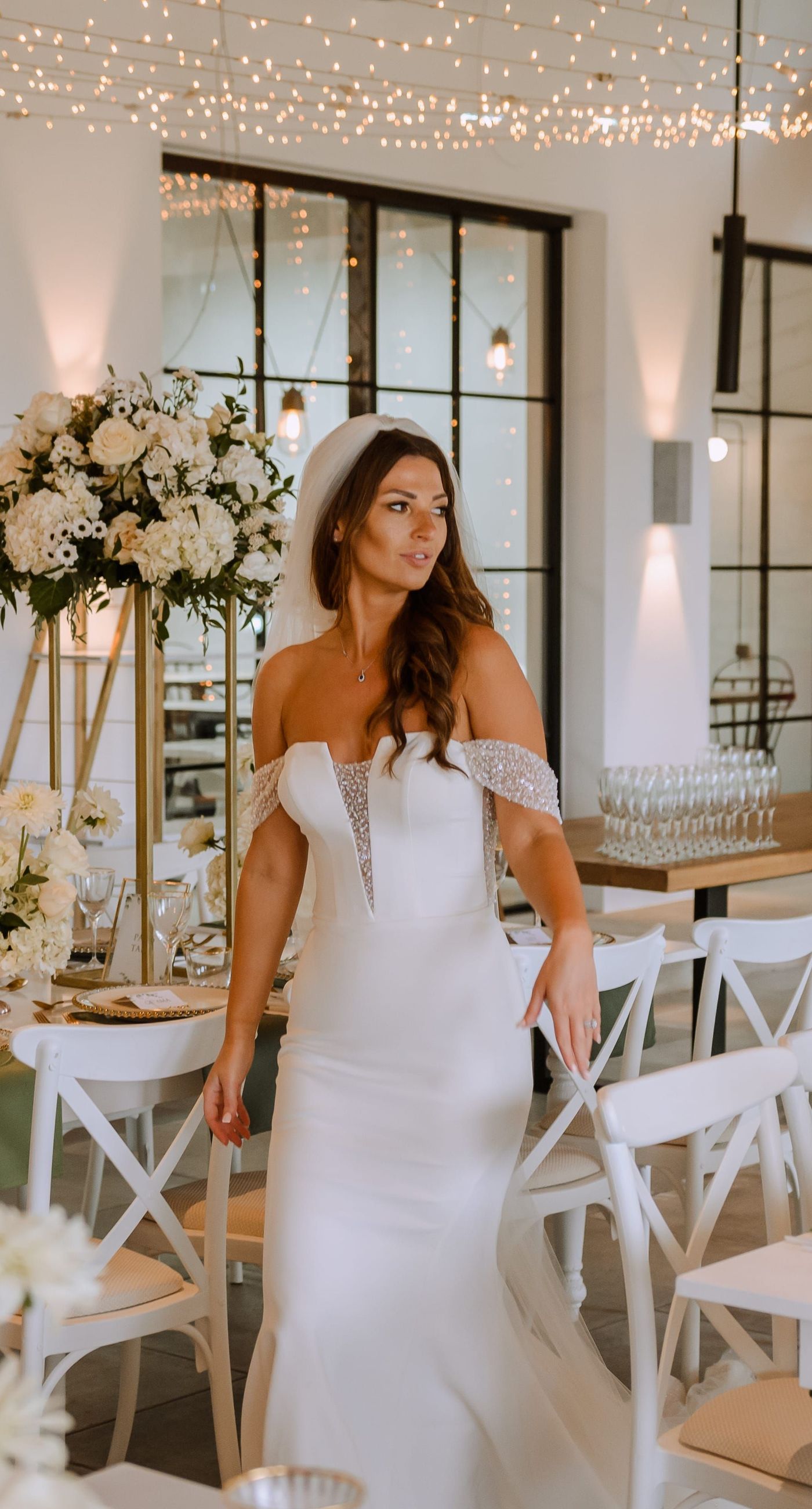 Christine & Eduart - Under a delicate floral arch, adorned with lush white blossoms and greenery, stands a vision of elegance and romance. The gentle pastel hues of the surrounding florals beautifully complement the soft, ethereal ambiance of this enchanting scene. It feels as though nature itself has been curated to frame a moment of serene connection, blending seamlessly into a verdant backdrop. The contrast of the bride's exquisite, flowing gown with the groom's tailored, modern attire in shades of emerald and white speaks volumes of both tradition and contemporary flair. This work captures an essence of timeless beauty, harmoniously blending natural elements with sophisticated design. - Photo 4