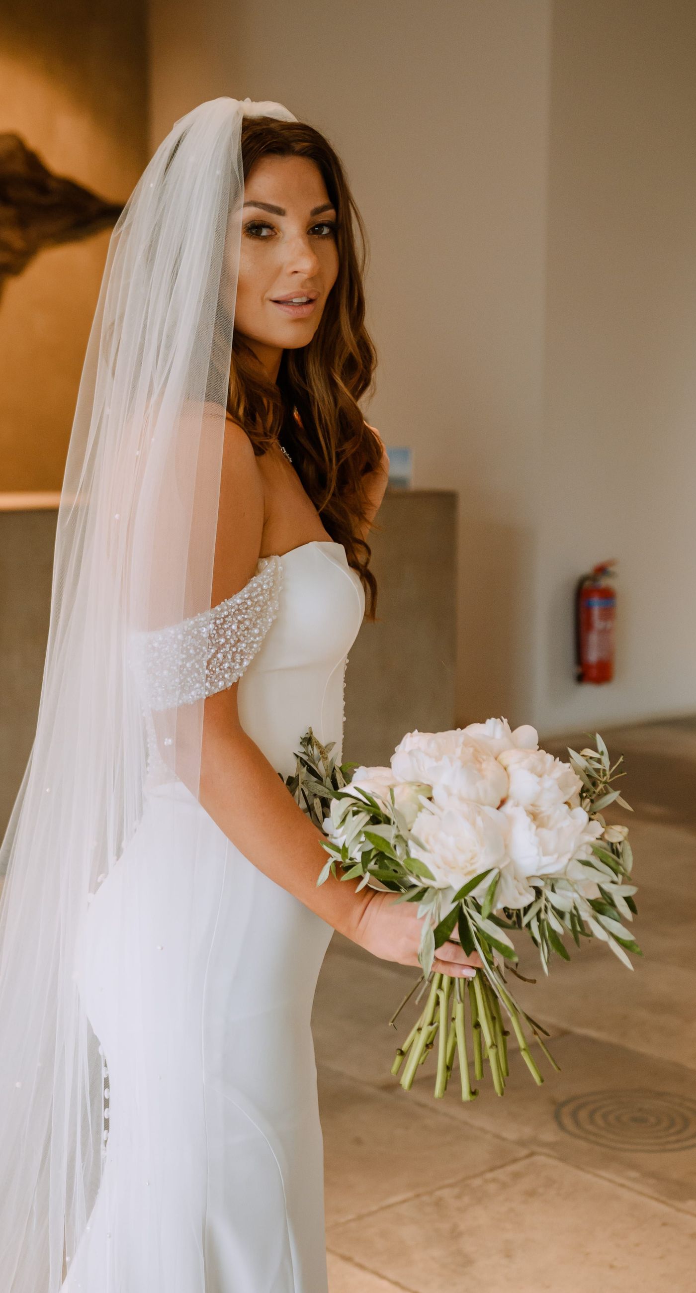 Christine & Eduart - Under a delicate floral arch, adorned with lush white blossoms and greenery, stands a vision of elegance and romance. The gentle pastel hues of the surrounding florals beautifully complement the soft, ethereal ambiance of this enchanting scene. It feels as though nature itself has been curated to frame a moment of serene connection, blending seamlessly into a verdant backdrop. The contrast of the bride's exquisite, flowing gown with the groom's tailored, modern attire in shades of emerald and white speaks volumes of both tradition and contemporary flair. This work captures an essence of timeless beauty, harmoniously blending natural elements with sophisticated design. - Photo 3