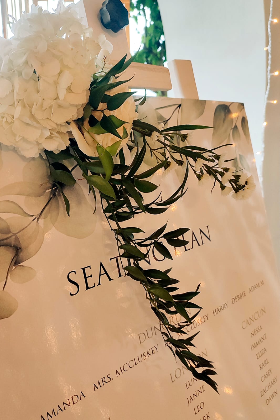 Christine & Eduart - Under a delicate floral arch, adorned with lush white blossoms and greenery, stands a vision of elegance and romance. The gentle pastel hues of the surrounding florals beautifully complement the soft, ethereal ambiance of this enchanting scene. It feels as though nature itself has been curated to frame a moment of serene connection, blending seamlessly into a verdant backdrop. The contrast of the bride's exquisite, flowing gown with the groom's tailored, modern attire in shades of emerald and white speaks volumes of both tradition and contemporary flair. This work captures an essence of timeless beauty, harmoniously blending natural elements with sophisticated design. - Photo 10