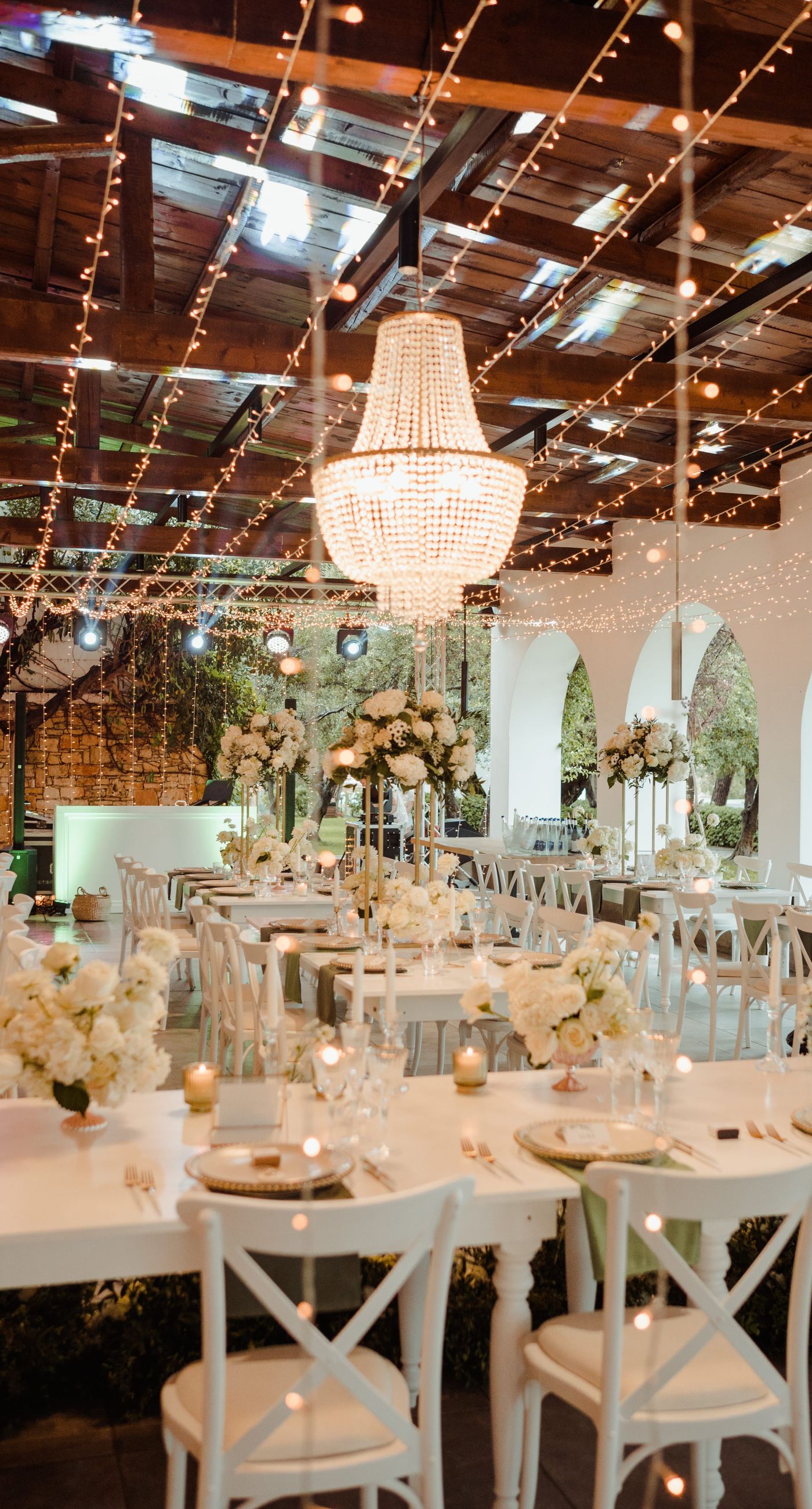 Christine & Eduart - Under a delicate floral arch, adorned with lush white blossoms and greenery, stands a vision of elegance and romance. The gentle pastel hues of the surrounding florals beautifully complement the soft, ethereal ambiance of this enchanting scene. It feels as though nature itself has been curated to frame a moment of serene connection, blending seamlessly into a verdant backdrop. The contrast of the bride's exquisite, flowing gown with the groom's tailored, modern attire in shades of emerald and white speaks volumes of both tradition and contemporary flair. This work captures an essence of timeless beauty, harmoniously blending natural elements with sophisticated design. - Photo 8