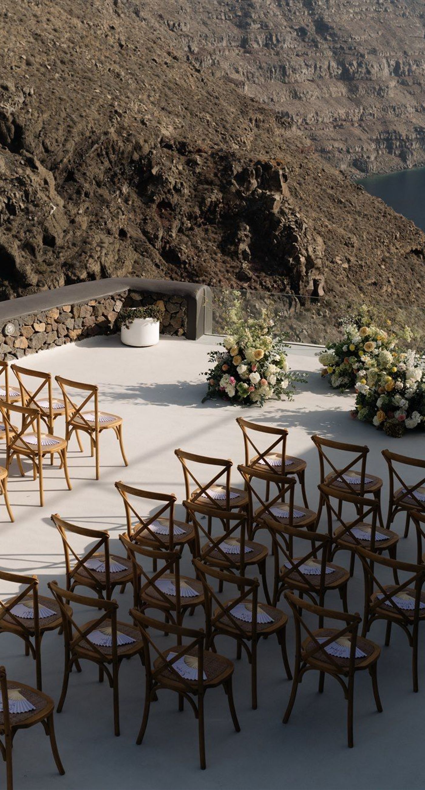 Courtney& Andrew - Bathed in the soft glow of a mountain backdrop, the scene captures a whimsical celebration of love. Soft white and blush rose petals float gently through the air, complementing the serene elegance of a bride in off-shoulder ivory silk and a groom in a classic black suit and tan trousers. The wooden chairs and delicate floral arrangements echo a natural, rustic charm, while the joyful guests add a vibrant energy. This portfolio piece beautifully encapsulates the essence of romantic bliss and harmonious design, set against nature's serene canvas. - Photo 1