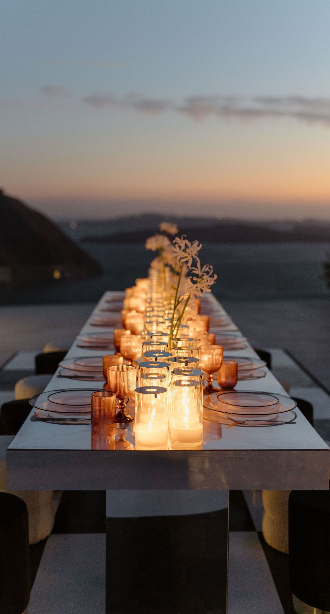 Emily & liam - In this exquisite scene, a couple stands in an ethereal embrace on a glass platform, surrounded by delicate blossoms that mirror the elegance of a sunlit seascape. The subdued pastels of the sunset wash gently over the horizon, casting a serene glow upon the couple and the blooms, creating a harmonious symphony of colors and emotions. The gracefully arranged white flowers echo timeless beauty and sophistication, set against the tranquil backdrop of a distant island. This stunning tableau invites you into a world where nature and romance converge seamlessly, an ideal representation for any florist's portfolio that values artistry and grace. - Photo 8