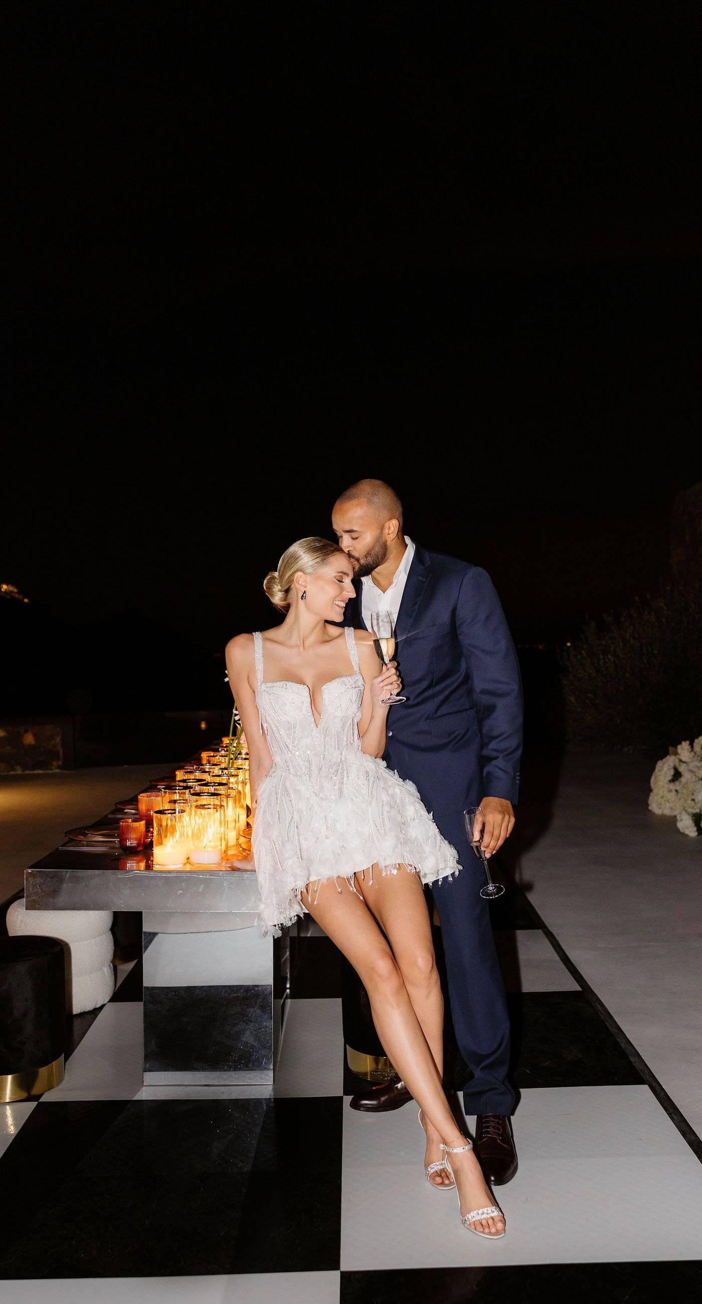 Emily & liam - In this exquisite scene, a couple stands in an ethereal embrace on a glass platform, surrounded by delicate blossoms that mirror the elegance of a sunlit seascape. The subdued pastels of the sunset wash gently over the horizon, casting a serene glow upon the couple and the blooms, creating a harmonious symphony of colors and emotions. The gracefully arranged white flowers echo timeless beauty and sophistication, set against the tranquil backdrop of a distant island. This stunning tableau invites you into a world where nature and romance converge seamlessly, an ideal representation for any florist's portfolio that values artistry and grace. - Photo 9