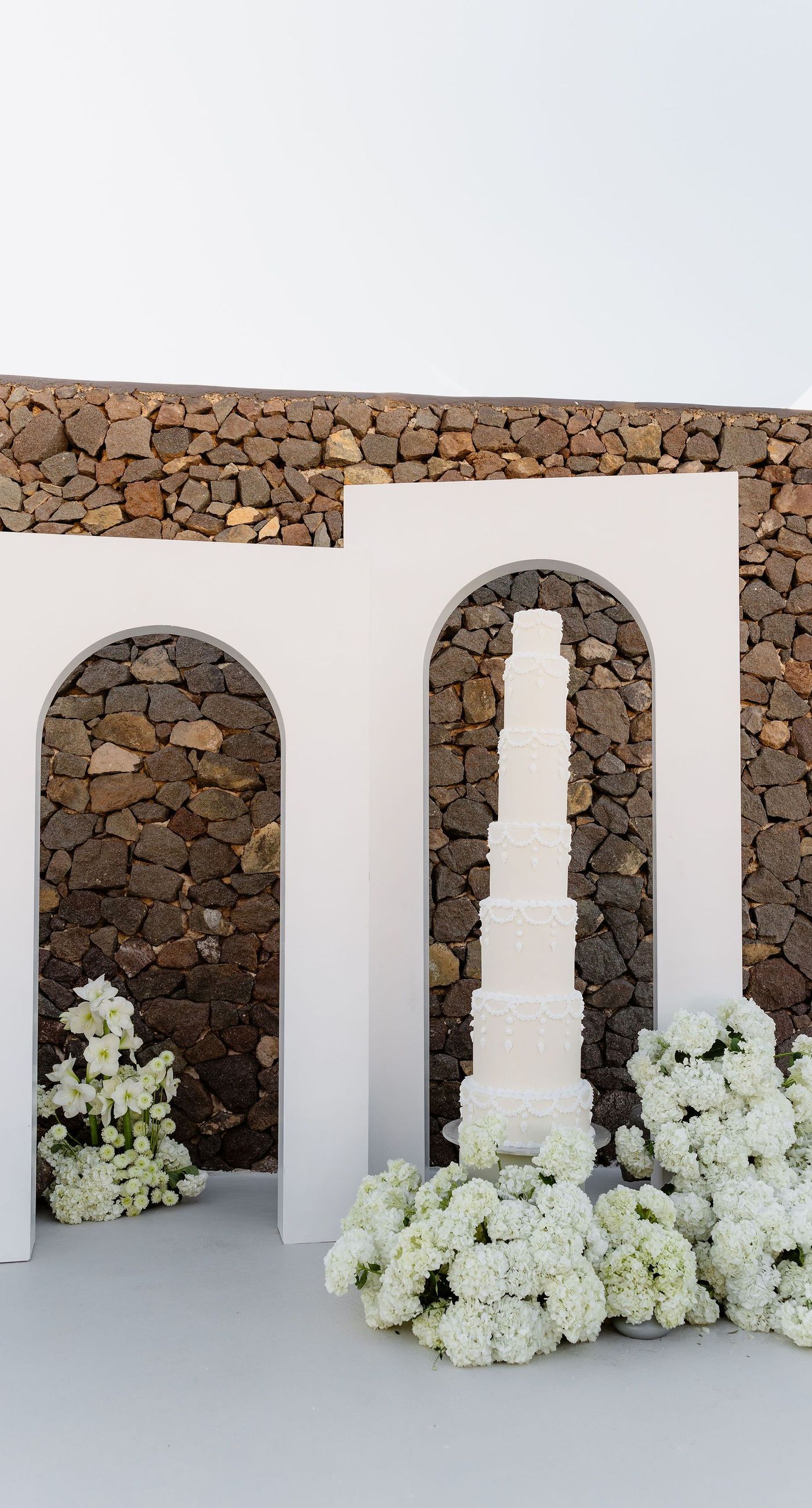 Emily & liam - In this exquisite scene, a couple stands in an ethereal embrace on a glass platform, surrounded by delicate blossoms that mirror the elegance of a sunlit seascape. The subdued pastels of the sunset wash gently over the horizon, casting a serene glow upon the couple and the blooms, creating a harmonious symphony of colors and emotions. The gracefully arranged white flowers echo timeless beauty and sophistication, set against the tranquil backdrop of a distant island. This stunning tableau invites you into a world where nature and romance converge seamlessly, an ideal representation for any florist's portfolio that values artistry and grace. - Photo 3