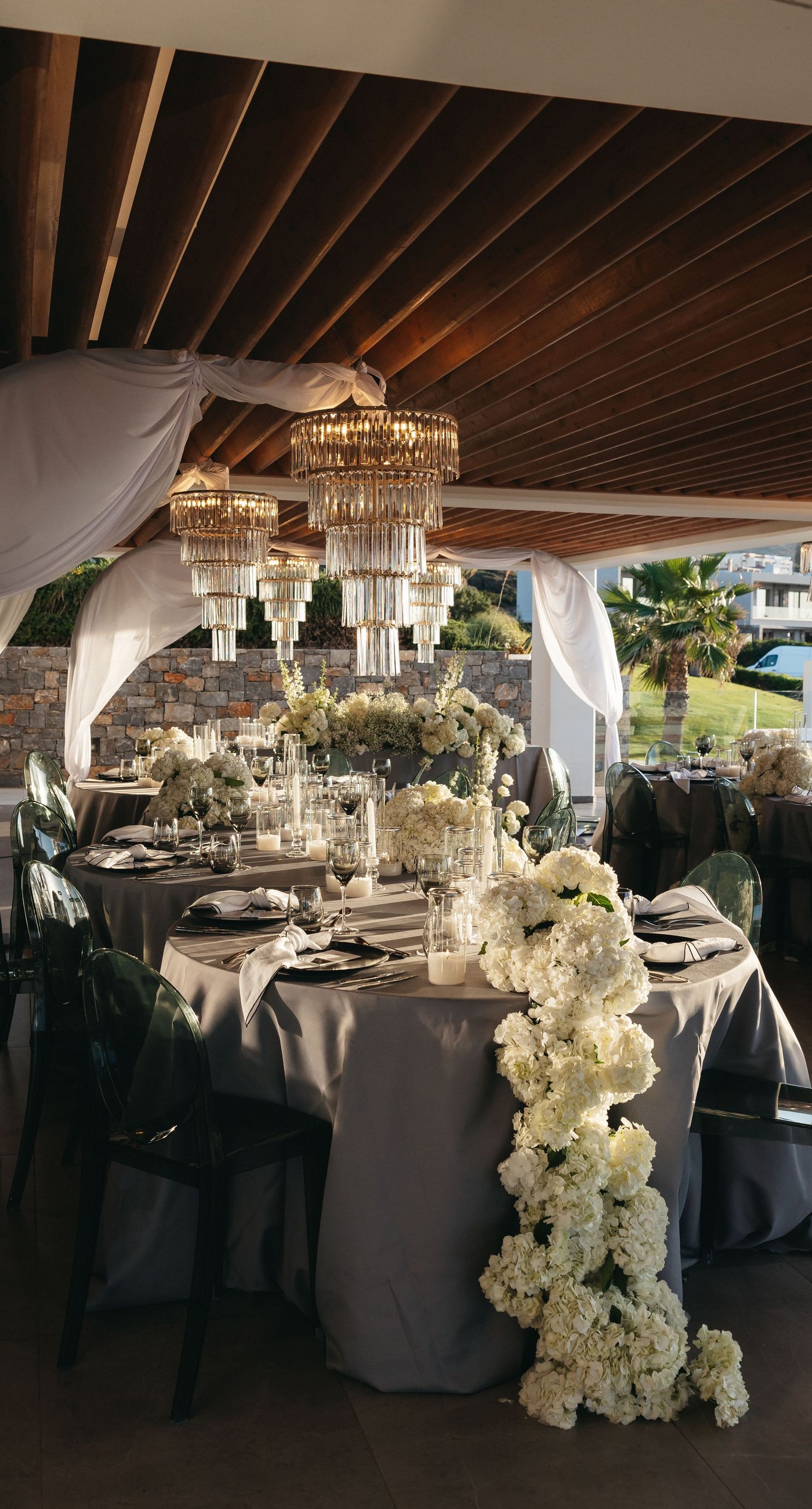 Holly & Mark - In a symphony of elegance and romance, this floral masterpiece frames an intimate moment beneath a brilliant blue sky. The archway, adorned with lush clusters of pristine white blooms and delicate baby's breath, creates a dreamy, ethereal backdrop that captures the essence of sophistication and serenity. The reflective surface beneath adds a touch of modernity, while the gentle ocean breeze seems to whisper promises of a new beginning. This harmonious blend of nature’s finest elements crafts a breathtaking scene, perfect for any discerning couple seeking a timeless and enchanting setting for their special day. - Photo 6