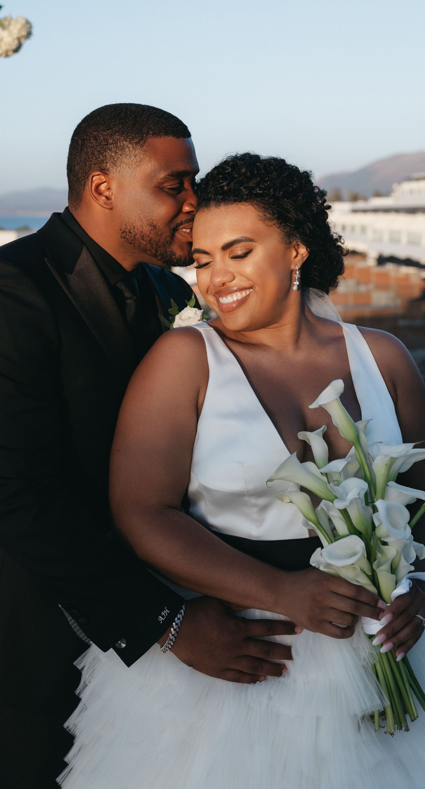 Holly & Mark - In a symphony of elegance and romance, this floral masterpiece frames an intimate moment beneath a brilliant blue sky. The archway, adorned with lush clusters of pristine white blooms and delicate baby's breath, creates a dreamy, ethereal backdrop that captures the essence of sophistication and serenity. The reflective surface beneath adds a touch of modernity, while the gentle ocean breeze seems to whisper promises of a new beginning. This harmonious blend of nature’s finest elements crafts a breathtaking scene, perfect for any discerning couple seeking a timeless and enchanting setting for their special day. - Photo 5