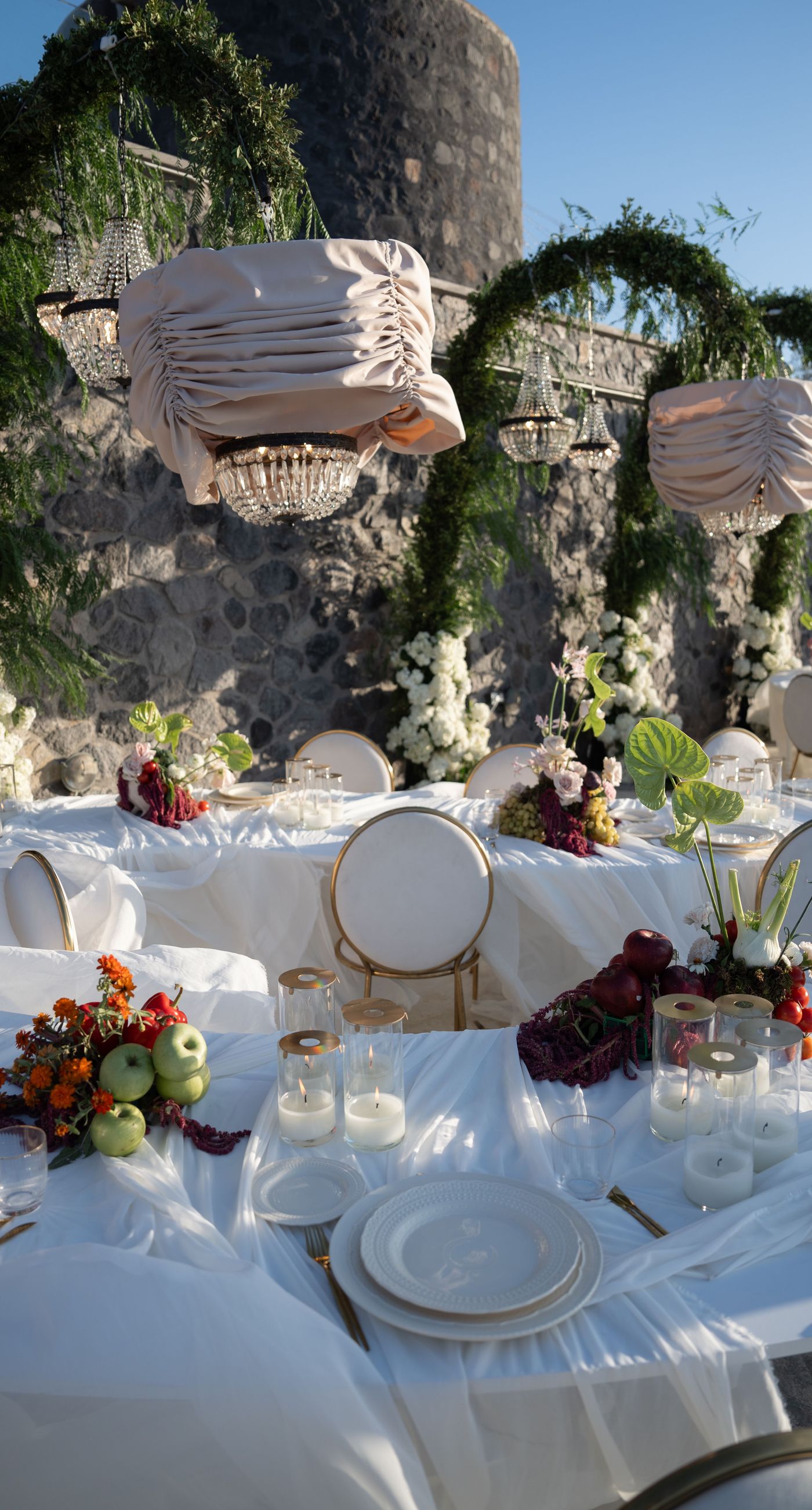 Isabella & Oliver - Under a clear blue sky, what unfolds is an ethereal expression of elegance and romance. The serene backdrop of vast, azure waters beautifully contrasts with the soft, delicate whites of the cascading petals, creating a scene both harmonious and enchanting. Meticulously arranged roses in gentle pinks and creams line the path, complementing the timeless lace and flowing structure of the bride's gown, while the groom's classic black suit adds a touch of refined sophistication. The graceful drapery, kissed by the gentle breeze, frames this moment of joy and forms a masterpiece of floral artistry, balancing nature's serenity with bridal grandeur. - Photo 8