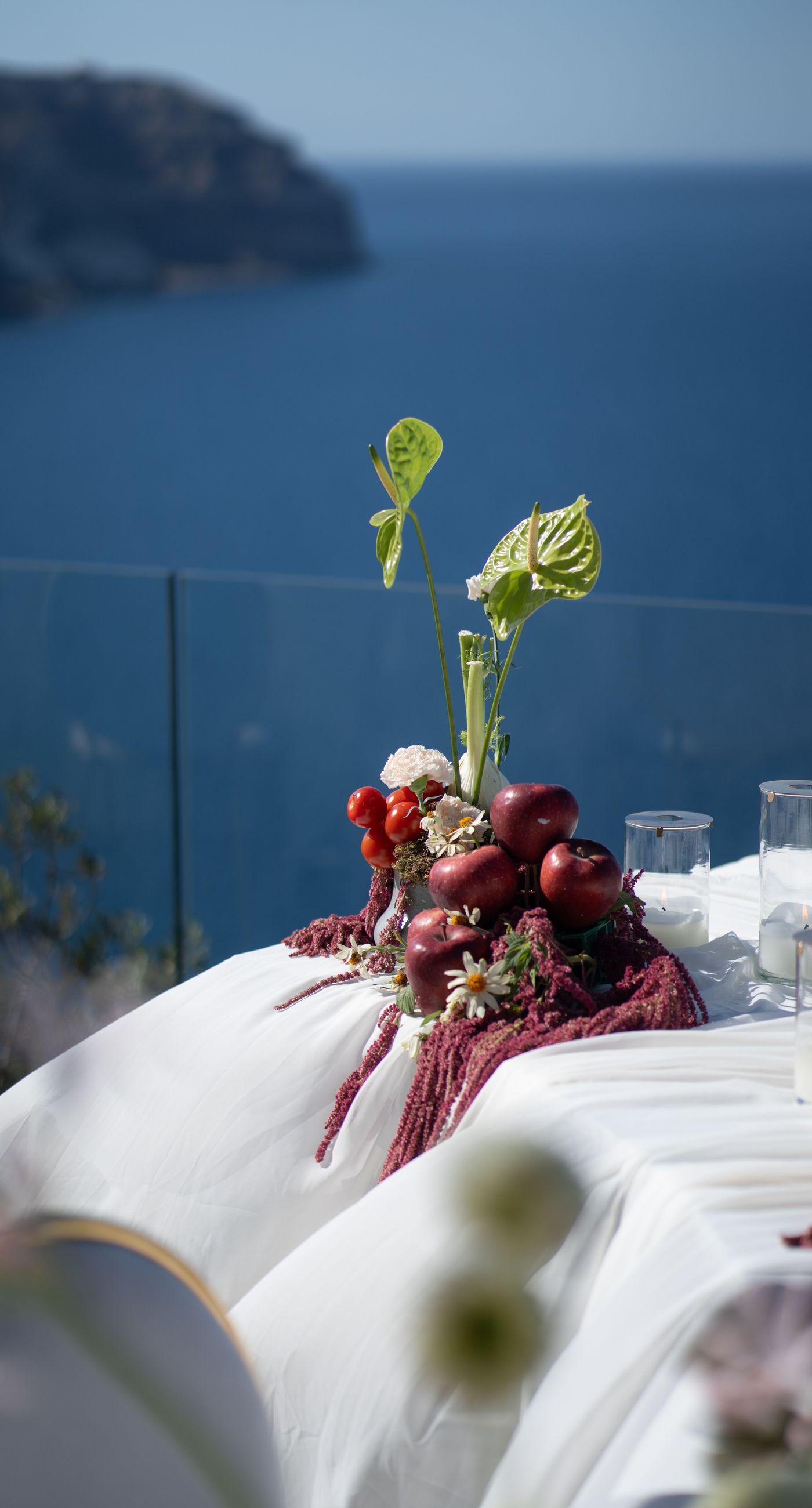 Isabella & Oliver - Under a clear blue sky, what unfolds is an ethereal expression of elegance and romance. The serene backdrop of vast, azure waters beautifully contrasts with the soft, delicate whites of the cascading petals, creating a scene both harmonious and enchanting. Meticulously arranged roses in gentle pinks and creams line the path, complementing the timeless lace and flowing structure of the bride's gown, while the groom's classic black suit adds a touch of refined sophistication. The graceful drapery, kissed by the gentle breeze, frames this moment of joy and forms a masterpiece of floral artistry, balancing nature's serenity with bridal grandeur. - Photo 15