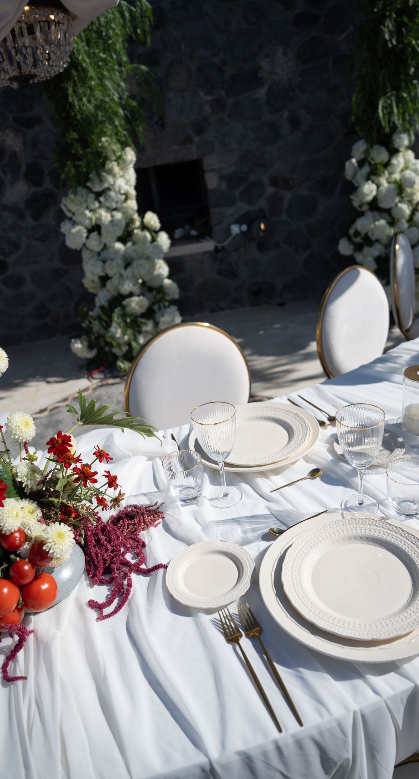 Isabella & Oliver - Under a clear blue sky, what unfolds is an ethereal expression of elegance and romance. The serene backdrop of vast, azure waters beautifully contrasts with the soft, delicate whites of the cascading petals, creating a scene both harmonious and enchanting. Meticulously arranged roses in gentle pinks and creams line the path, complementing the timeless lace and flowing structure of the bride's gown, while the groom's classic black suit adds a touch of refined sophistication. The graceful drapery, kissed by the gentle breeze, frames this moment of joy and forms a masterpiece of floral artistry, balancing nature's serenity with bridal grandeur. - Photo 10