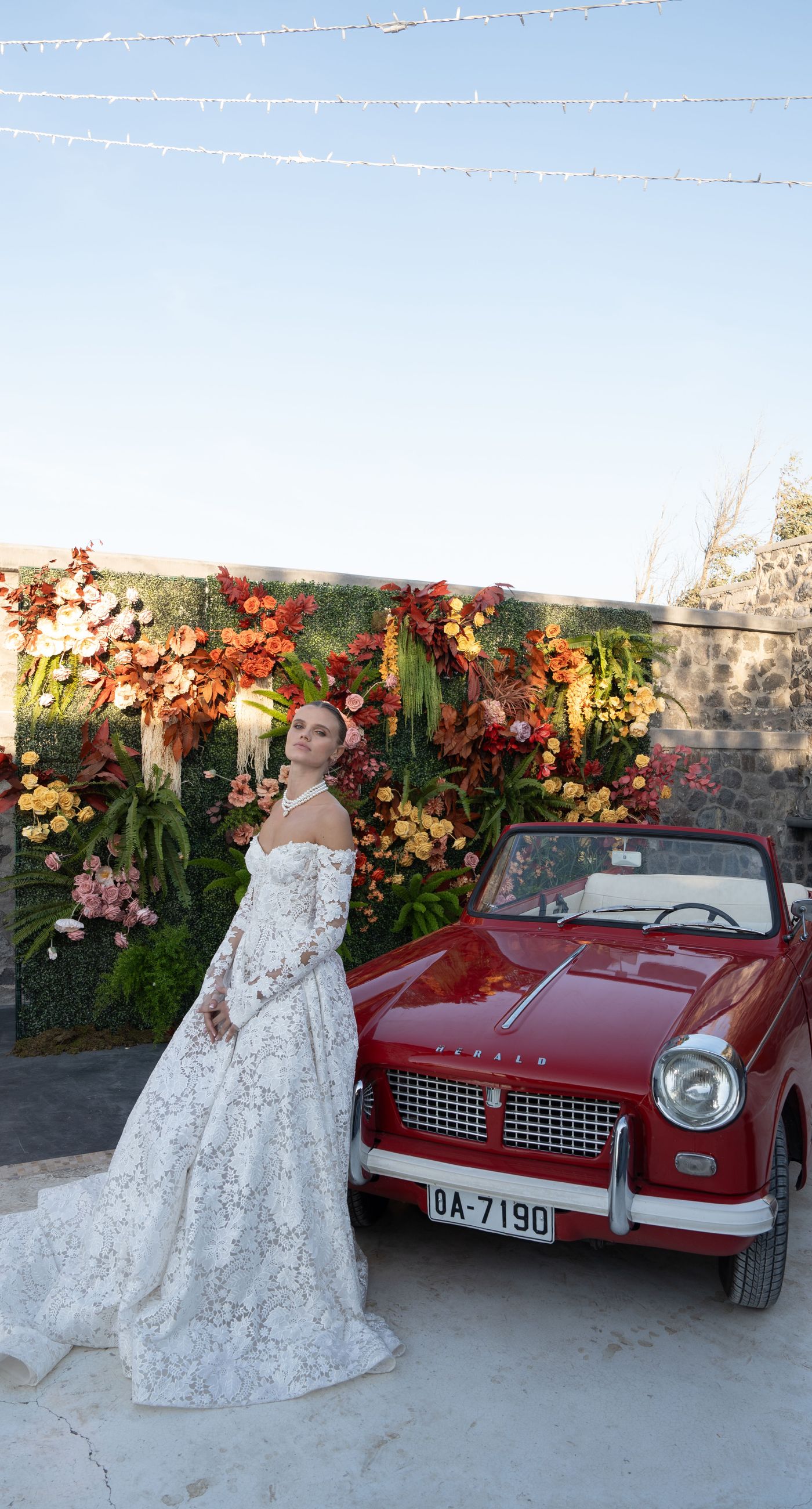 Isabella & Oliver - Under a clear blue sky, what unfolds is an ethereal expression of elegance and romance. The serene backdrop of vast, azure waters beautifully contrasts with the soft, delicate whites of the cascading petals, creating a scene both harmonious and enchanting. Meticulously arranged roses in gentle pinks and creams line the path, complementing the timeless lace and flowing structure of the bride's gown, while the groom's classic black suit adds a touch of refined sophistication. The graceful drapery, kissed by the gentle breeze, frames this moment of joy and forms a masterpiece of floral artistry, balancing nature's serenity with bridal grandeur. - Photo 5