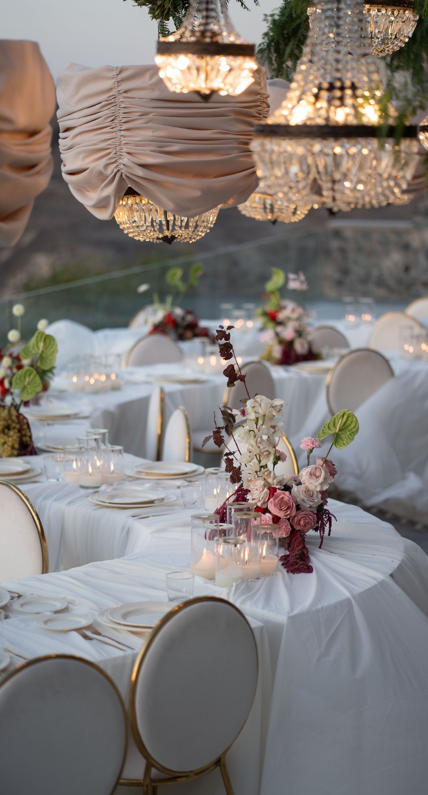 Isabella & Oliver - Under a clear blue sky, what unfolds is an ethereal expression of elegance and romance. The serene backdrop of vast, azure waters beautifully contrasts with the soft, delicate whites of the cascading petals, creating a scene both harmonious and enchanting. Meticulously arranged roses in gentle pinks and creams line the path, complementing the timeless lace and flowing structure of the bride's gown, while the groom's classic black suit adds a touch of refined sophistication. The graceful drapery, kissed by the gentle breeze, frames this moment of joy and forms a masterpiece of floral artistry, balancing nature's serenity with bridal grandeur. - Photo 13