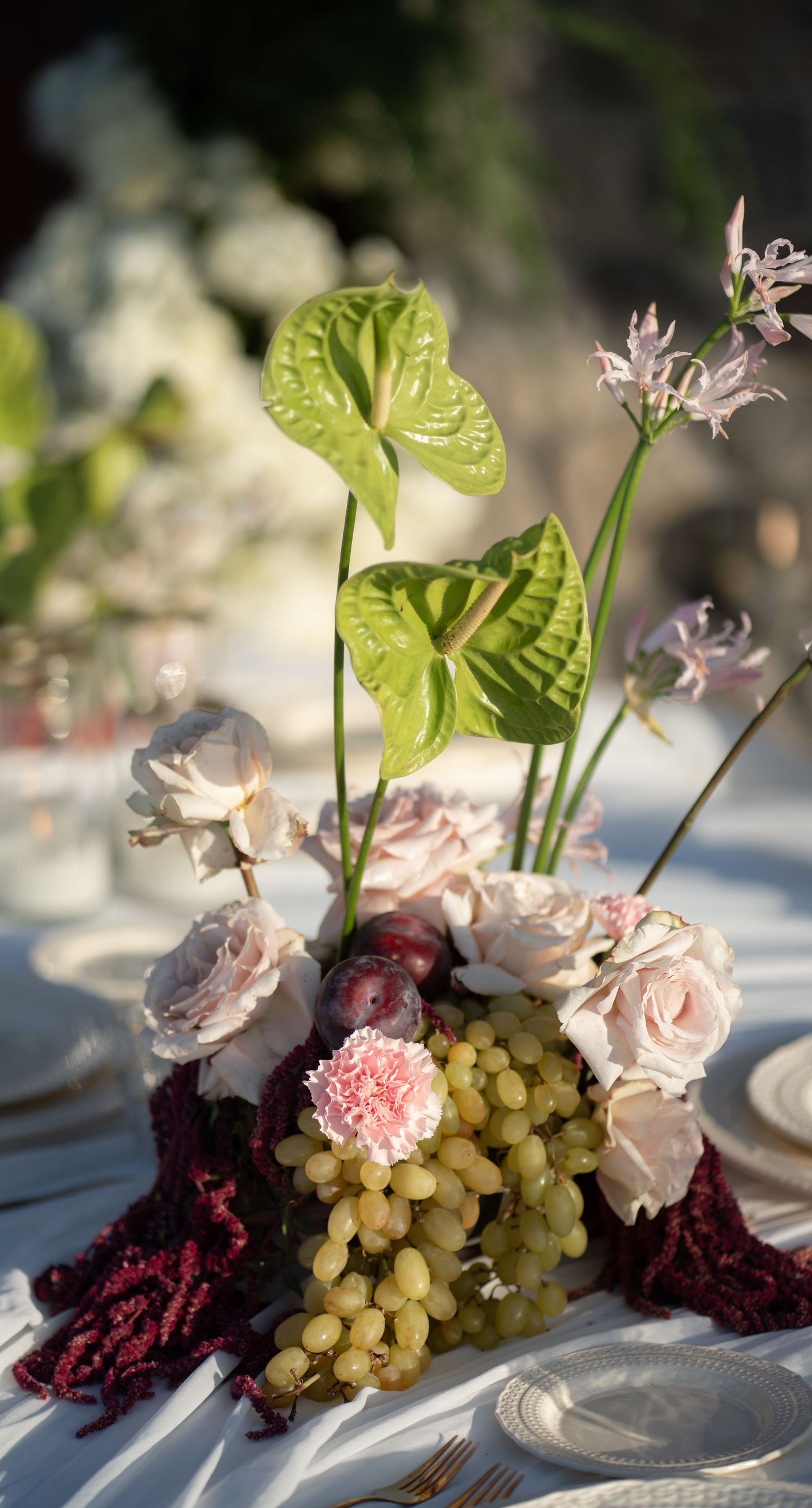 Isabella & Oliver - Under a clear blue sky, what unfolds is an ethereal expression of elegance and romance. The serene backdrop of vast, azure waters beautifully contrasts with the soft, delicate whites of the cascading petals, creating a scene both harmonious and enchanting. Meticulously arranged roses in gentle pinks and creams line the path, complementing the timeless lace and flowing structure of the bride's gown, while the groom's classic black suit adds a touch of refined sophistication. The graceful drapery, kissed by the gentle breeze, frames this moment of joy and forms a masterpiece of floral artistry, balancing nature's serenity with bridal grandeur. - Photo 12