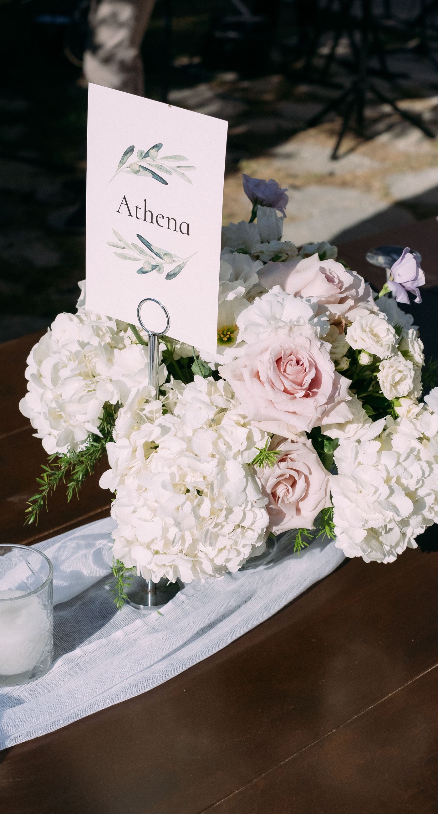 June & Tim - Beneath a lush canopy of greenery, a symphony of ivory and blush blooms cascades in a breathtaking floral arch. The delicate roses and verdant ferns intertwine effortlessly, creating a harmonious backdrop that exudes elegance and romance. The serene garden setting bathes the scene in soft, natural light, enhancing the ethereal beauty of the arrangement. The joyful expressions of the couple, captured in this radiant moment, complement the stunning florals with a vibrant energy. This captivating work reflects a masterful blend of nature's artistry and human emotion, making it an unforgettable statement in any portfolio. - Photo 7