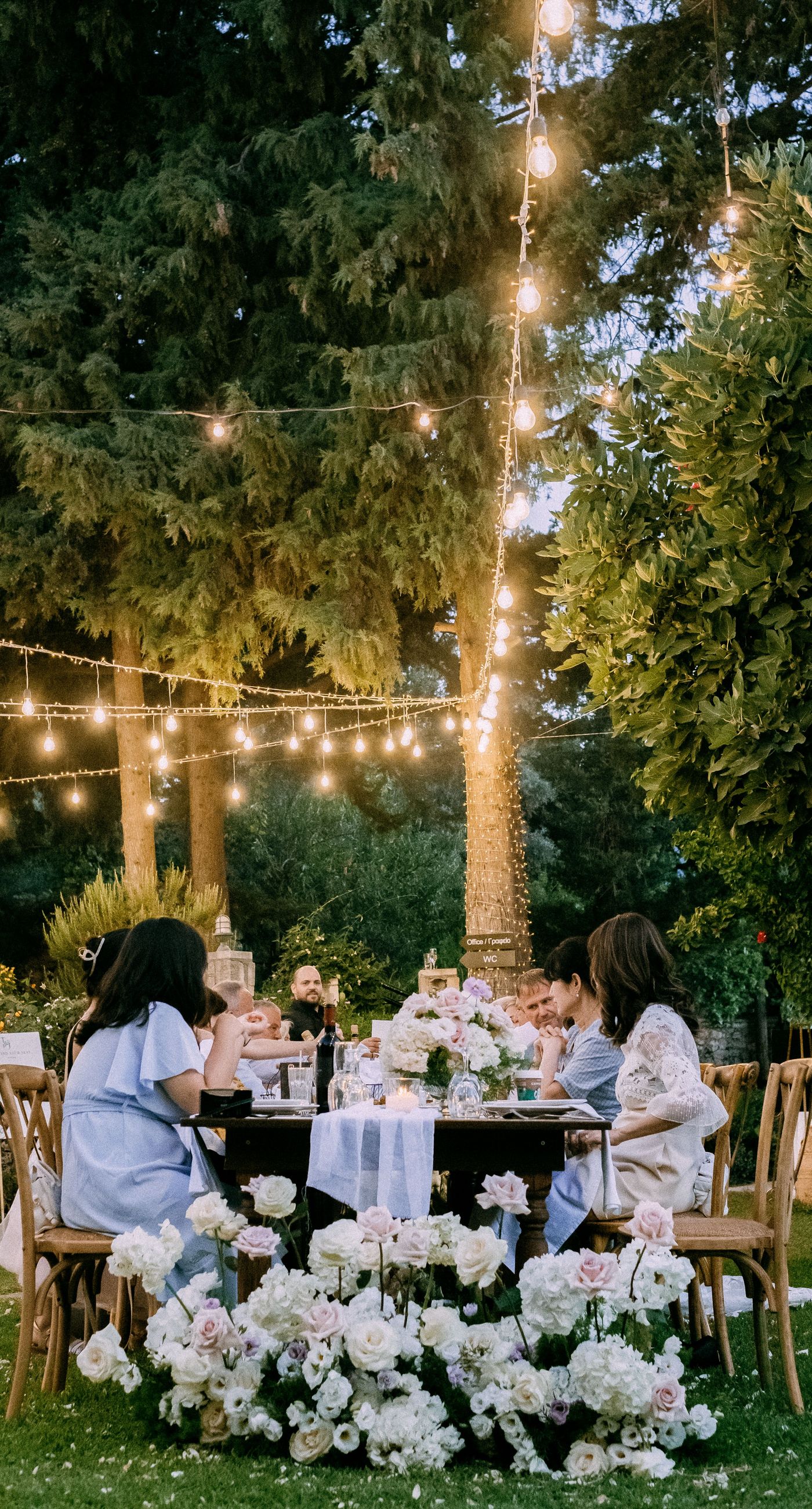June & Tim - Beneath a lush canopy of greenery, a symphony of ivory and blush blooms cascades in a breathtaking floral arch. The delicate roses and verdant ferns intertwine effortlessly, creating a harmonious backdrop that exudes elegance and romance. The serene garden setting bathes the scene in soft, natural light, enhancing the ethereal beauty of the arrangement. The joyful expressions of the couple, captured in this radiant moment, complement the stunning florals with a vibrant energy. This captivating work reflects a masterful blend of nature's artistry and human emotion, making it an unforgettable statement in any portfolio. - Photo 9