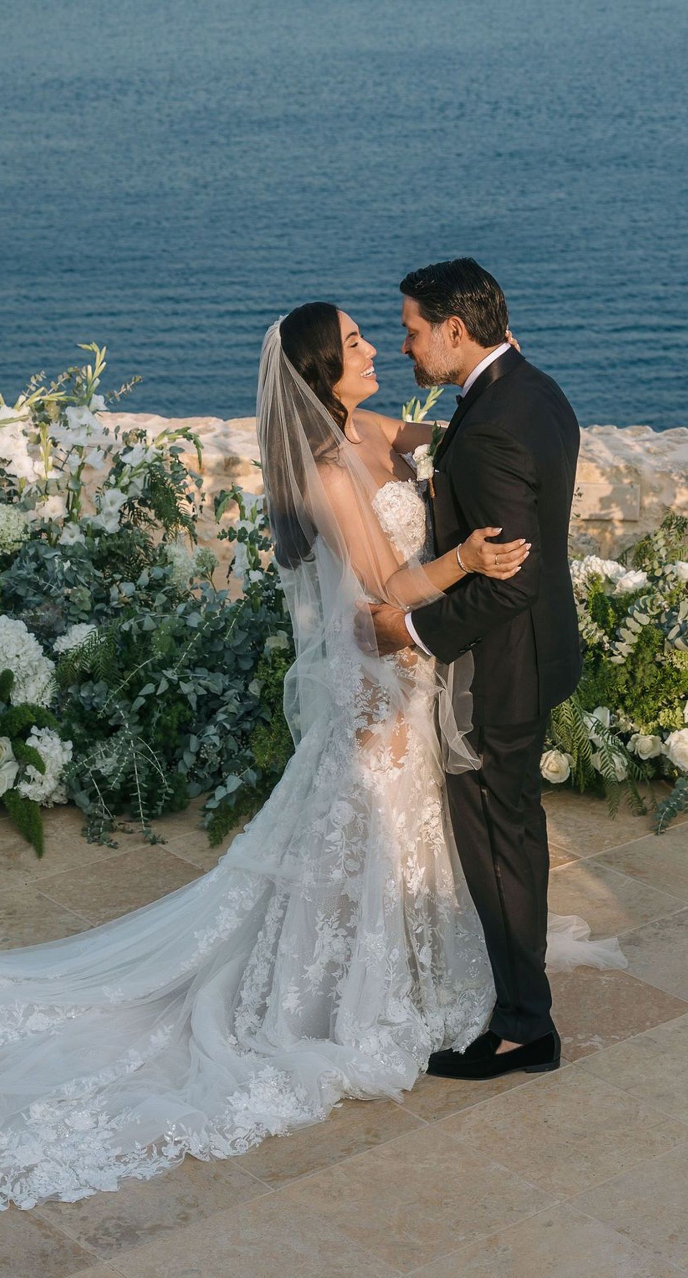 Kala & Kerwin - Bathed in the warm glow of a setting sun, the bouquet of creamy white blooms and eucalyptus whispers elegance and romance. It complements the ethereal lace details of the attire, creating a harmonious blend of textures and colors. The backdrop of rustic stone steps hints at a location where nature and romance intertwine seamlessly, offering a timeless, serene beauty. This work encapsulates a moment of profound connection and grace, emphasizing the pure emotional essence captured on a special day. - Photo 1