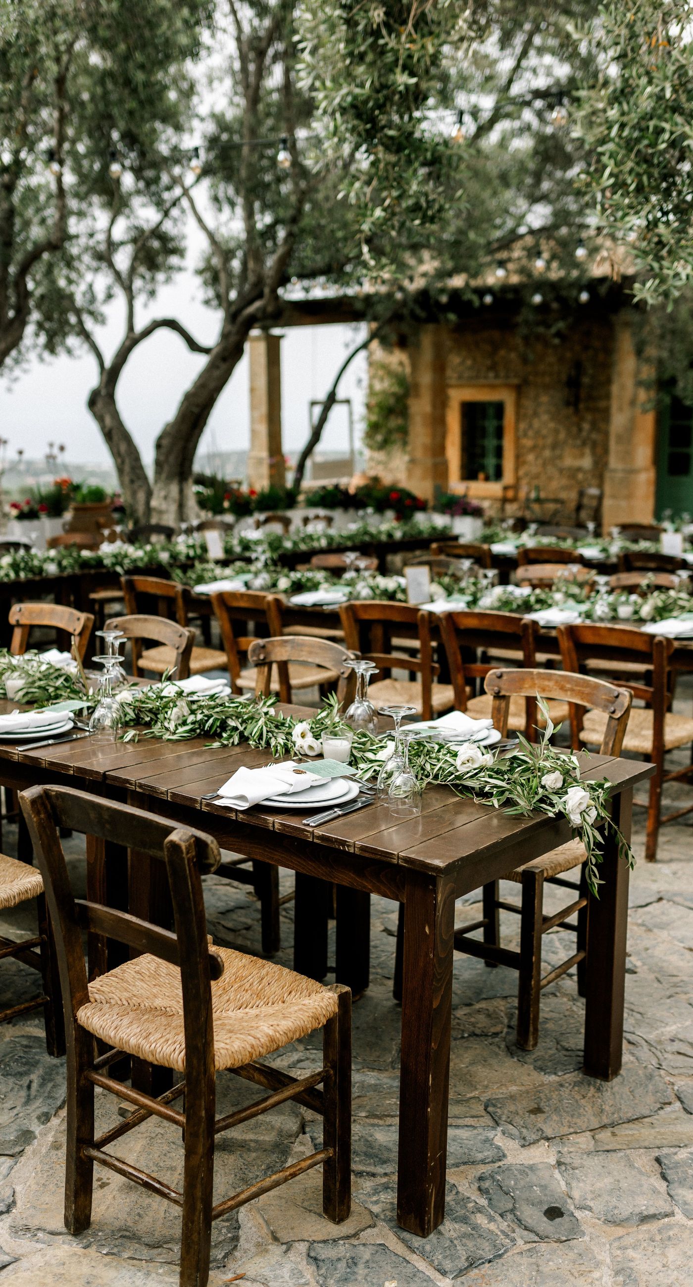 Katherine & Adam - Nestled within the lush, sprawling rows of a vineyard, the scene captures an exquisite moment of romance and elegance. The verdant landscape creates a serene backdrop, perfectly complementing the delicate whites and soft greens of the bride's bouquet. The interplay between the timeless black tuxedo and the pure white gown establishes a harmonious balance, inviting you into a world of classic beauty and serene intimacy. The gentle kiss shared amidst the verdant vines evokes a sense of rustic charm blended with refined grace, an ideal setting for a florist's artistry in capturing life's tender moments. - Photo 11