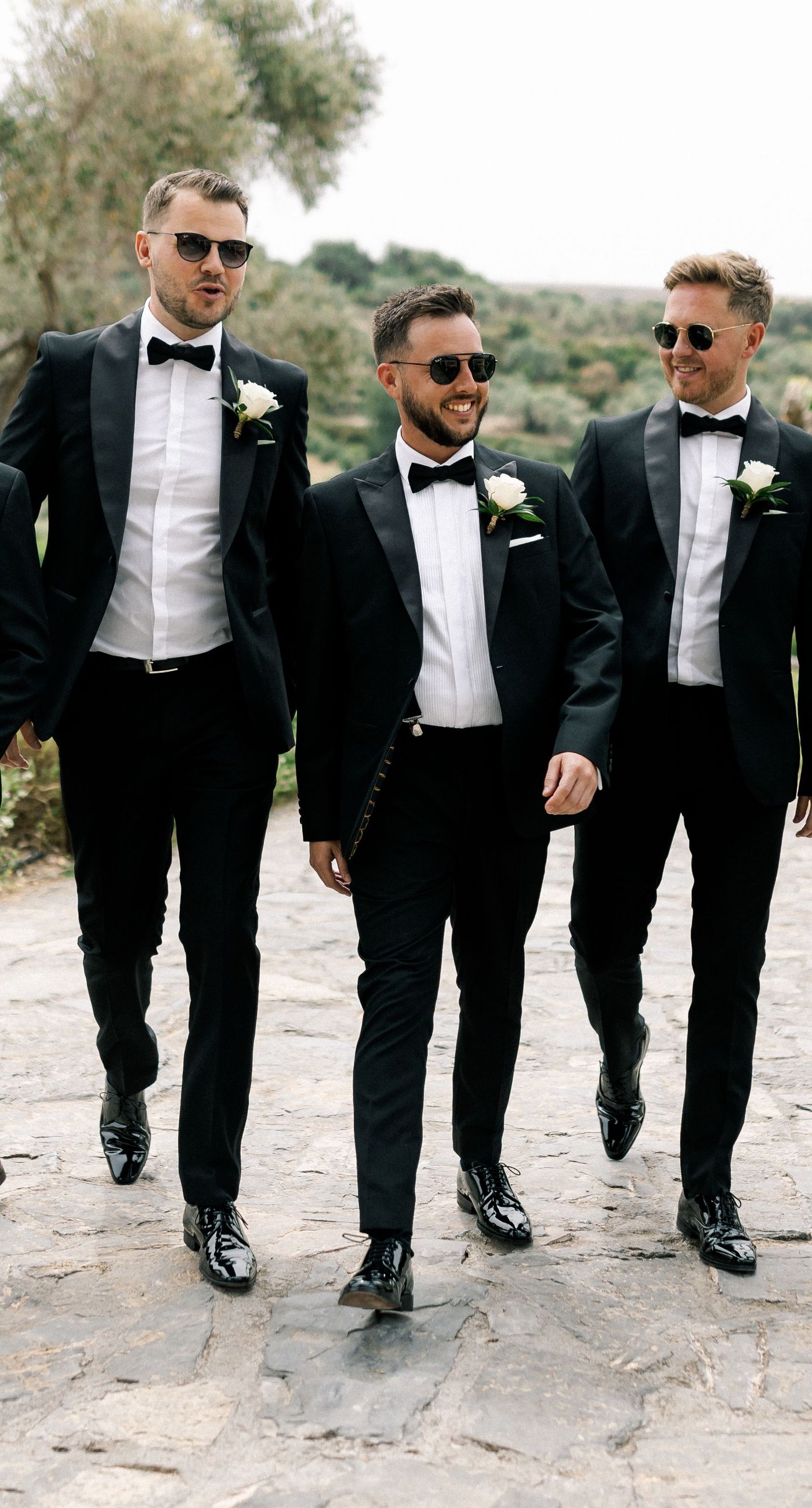 Katherine & Adam - Nestled within the lush, sprawling rows of a vineyard, the scene captures an exquisite moment of romance and elegance. The verdant landscape creates a serene backdrop, perfectly complementing the delicate whites and soft greens of the bride's bouquet. The interplay between the timeless black tuxedo and the pure white gown establishes a harmonious balance, inviting you into a world of classic beauty and serene intimacy. The gentle kiss shared amidst the verdant vines evokes a sense of rustic charm blended with refined grace, an ideal setting for a florist's artistry in capturing life's tender moments. - Photo 3