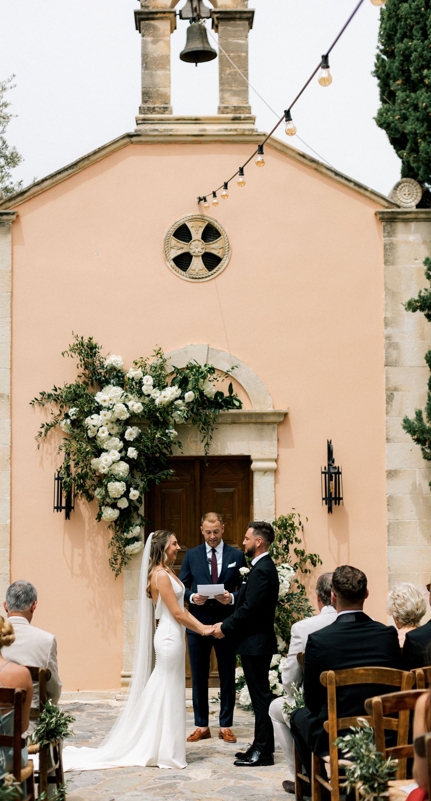Katherine & Adam - Nestled within the lush, sprawling rows of a vineyard, the scene captures an exquisite moment of romance and elegance. The verdant landscape creates a serene backdrop, perfectly complementing the delicate whites and soft greens of the bride's bouquet. The interplay between the timeless black tuxedo and the pure white gown establishes a harmonious balance, inviting you into a world of classic beauty and serene intimacy. The gentle kiss shared amidst the verdant vines evokes a sense of rustic charm blended with refined grace, an ideal setting for a florist's artistry in capturing life's tender moments. - Photo 5