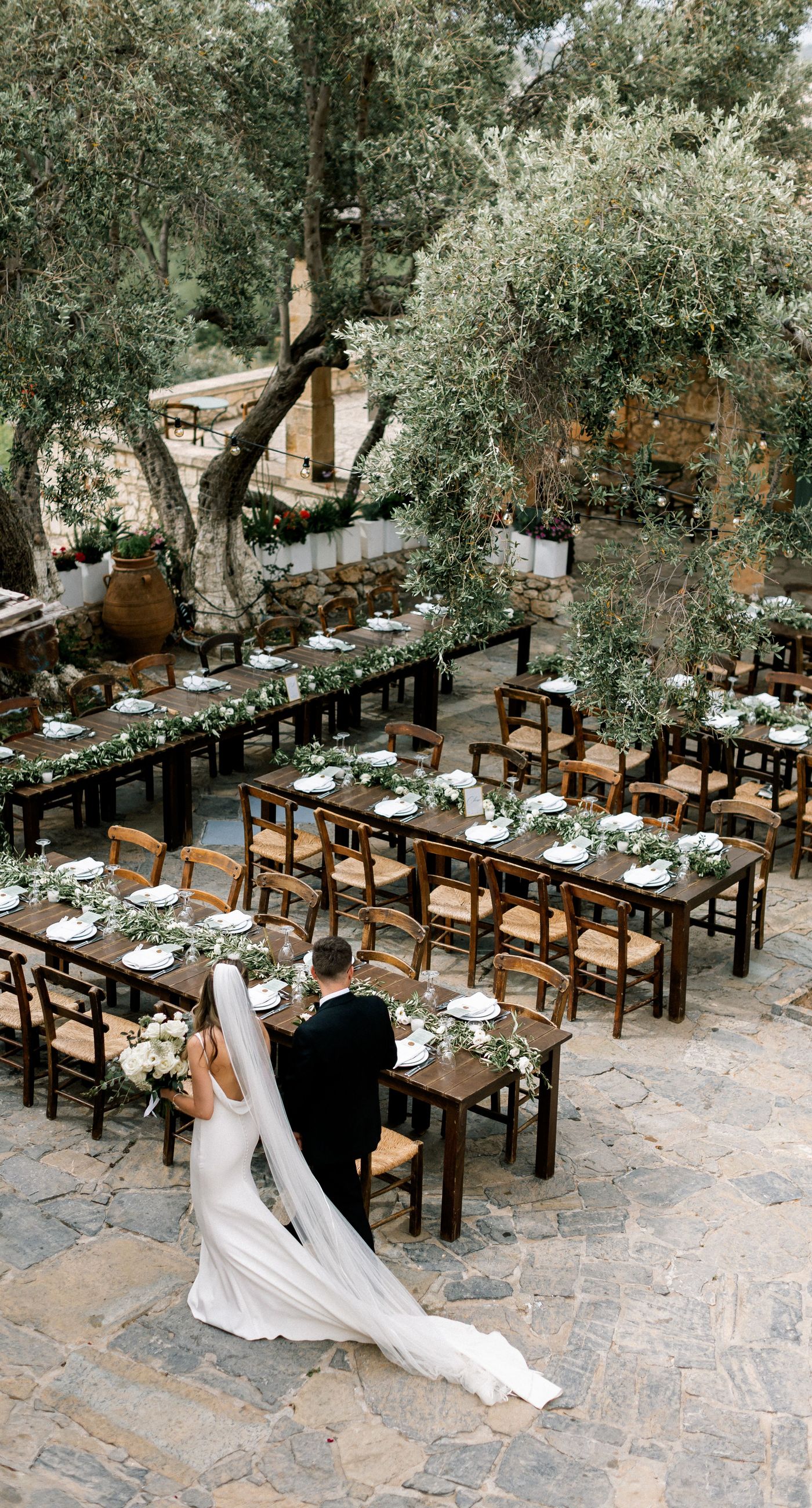 Katherine & Adam - Nestled within the lush, sprawling rows of a vineyard, the scene captures an exquisite moment of romance and elegance. The verdant landscape creates a serene backdrop, perfectly complementing the delicate whites and soft greens of the bride's bouquet. The interplay between the timeless black tuxedo and the pure white gown establishes a harmonious balance, inviting you into a world of classic beauty and serene intimacy. The gentle kiss shared amidst the verdant vines evokes a sense of rustic charm blended with refined grace, an ideal setting for a florist's artistry in capturing life's tender moments. - Photo 10