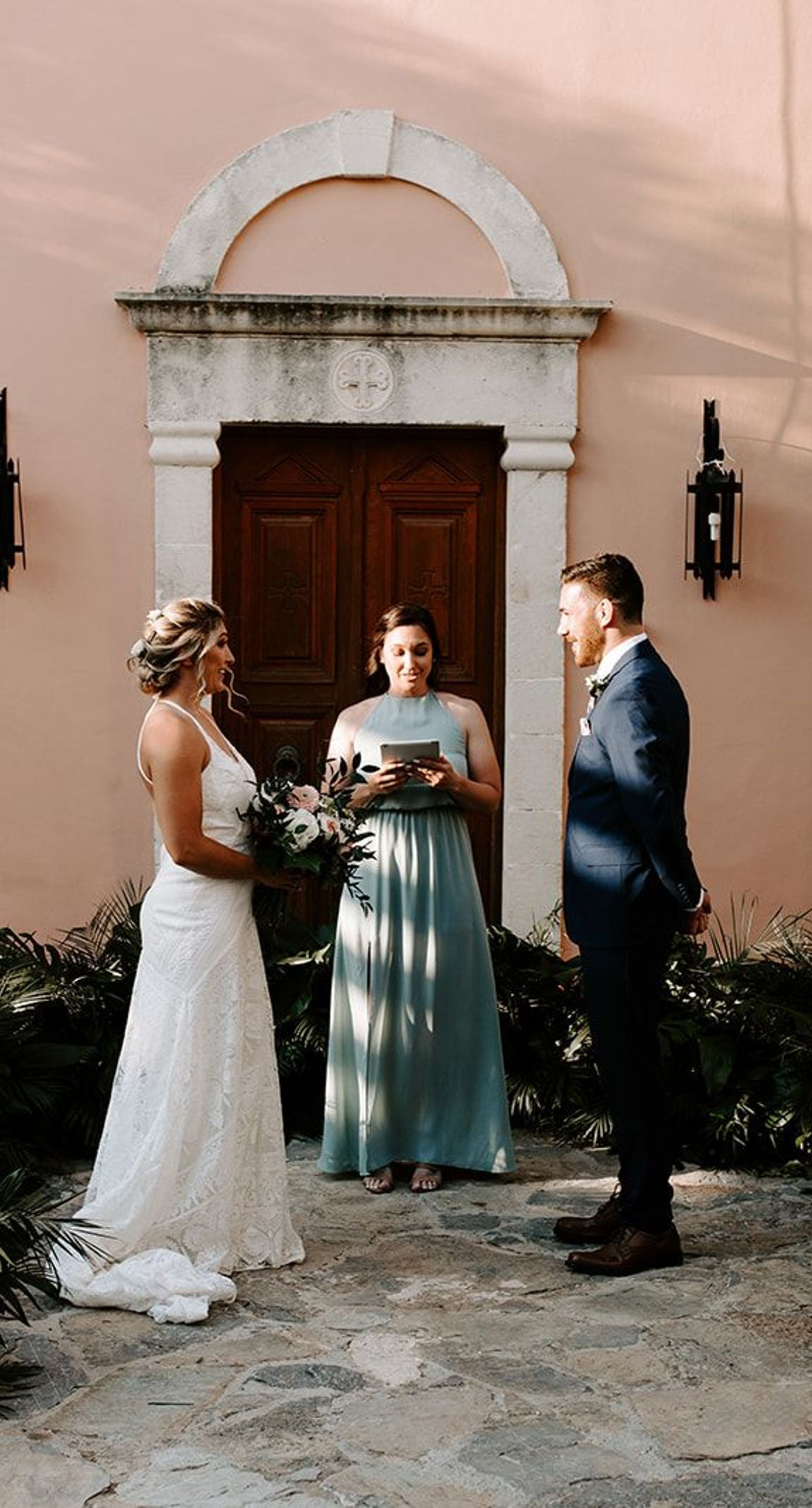 Ketty & Smith - In a symphony of soft pink hues and delicate floral arrangements, the romance of this work unfolds against a backdrop of timeless charm. The couple stands enveloped in a misty blush, their intimate embrace framed by an elegant stone archway, exuding elegance and warmth. The bride's bouquet, a harmonious blend of greenery and pastel blossoms, complements the sophisticated navy of the groom's suit, while the gentle palette of the setting evokes an ethereal, dreamlike quality. Every element is curated with graceful precision, creating a tapestry of love and beauty that is both refined and captivating. - Photo 5