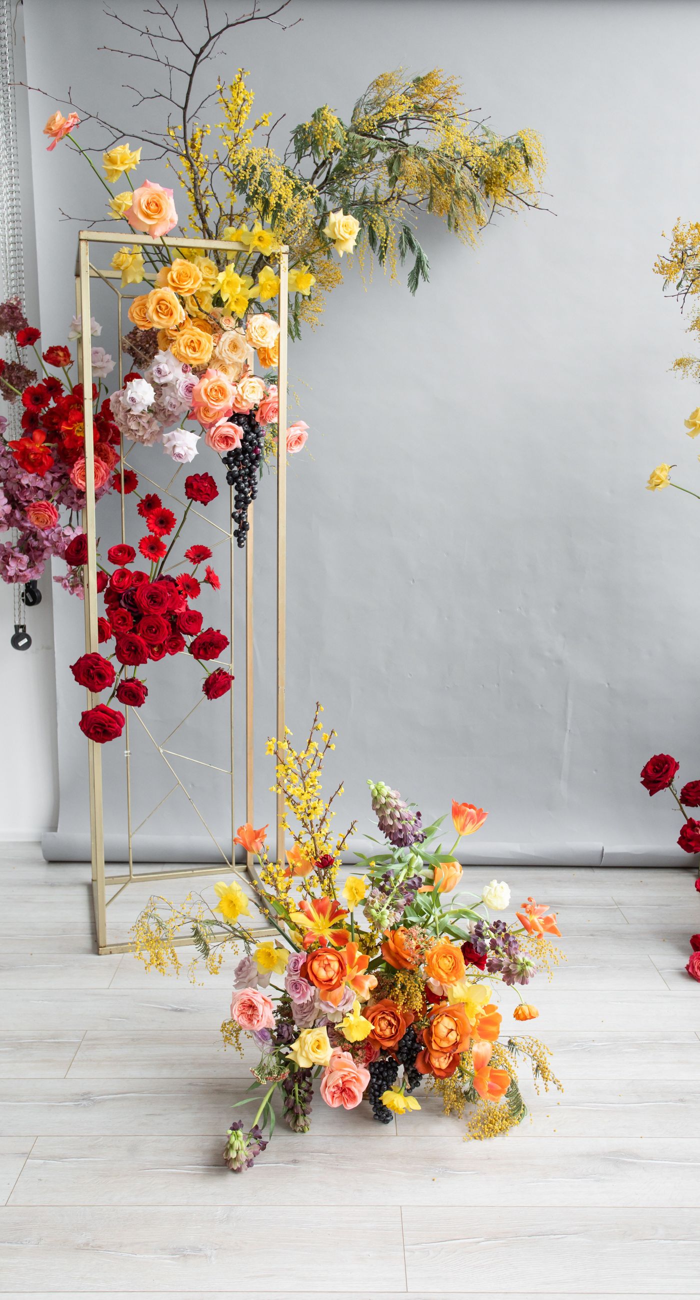 Medieval Dinner - In a symphony of colors, this floral arrangement weaves together vibrancy and elegance, creating an aesthetic that feels both timeless and contemporary. The vivid reds, yellows, and oranges of the blooms contrast strikingly against a soft, neutral backdrop, while a rich, wine-colored robe adds a touch of opulence. Surrounded by a lush abundance of fruits and elegant tableware, the setting evokes a sense of refined abundance, as if captured in a modern-day still life. The arrangement harmoniously balances the natural and the curated, transforming the space into a living work of art, and serving as a striking centerpiece for a florist's creative portfolio.
 - Photo 1