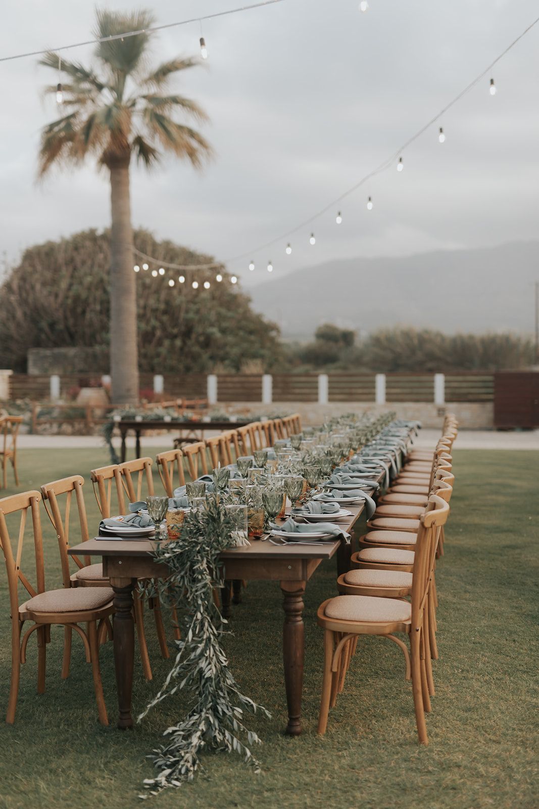 Mitchell & Antoinnette - In a moment that captures the essence of serene elegance, a couple stands poised against the backdrop of a distant shoreline. Her flowing white gown, complemented by his classic black tuxedo, exudes timeless sophistication. The gentle cascade of her dark locks adds a soft contrast to the bright purity of her dress, embodying a harmonious balance of light and dark. The subtle embrace and their intertwined fingers speak a silent language of affection, creating an intimate tableau. This tranquil scene, bathed in natural light and framed by the lush greenery beyond, evokes a sense of calm and enduring romance—an ideal accompaniment to any floral arrangement that seeks to encapsulate love in its most genuine form. - Photo 6