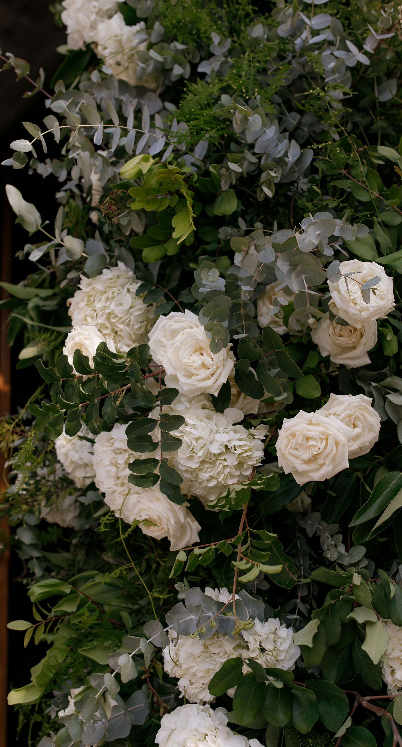 Natalia & John  - Amidst a cascade of ivory roses and lush greenery, an elegantly composed scene unfolds, embodying a timeless romance. The bride, draped in a voluminous white gown, holds a delicate bouquet of blooms that mirrors the floral splendor surrounding her. The groom, in classic black tie, complements the serene palette with a touch of timeless elegance. This artistic composition brings together the soft whispers of petals and the gentle embrace of forgotten days, creating a vibrant harmony between nature's charm and heartfelt human moments. The florals, artfully arranged, create an enchanting backdrop that speaks of new beginnings and enduring beauty. - Photo 4