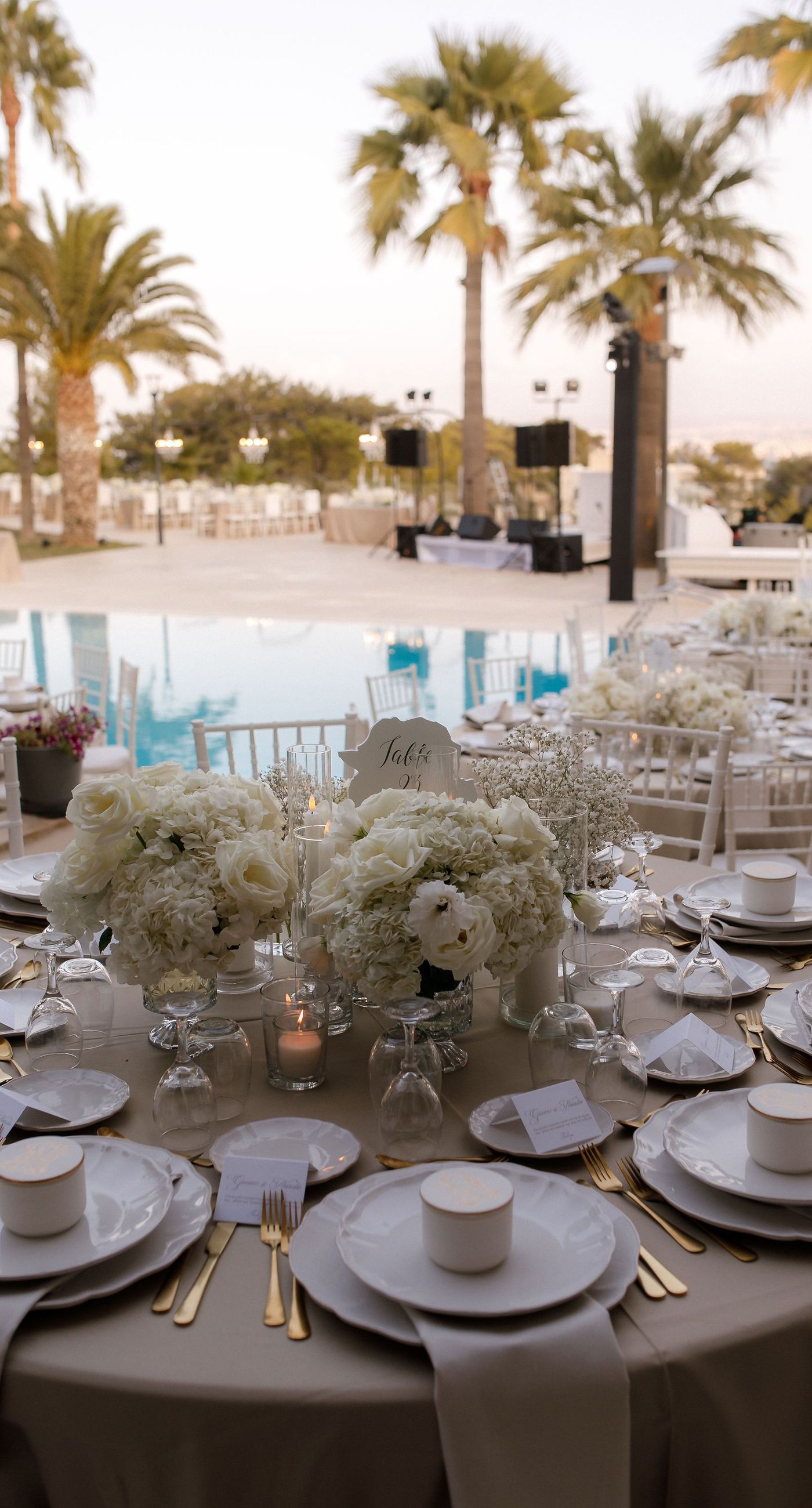 Natalia & John  - Amidst a cascade of ivory roses and lush greenery, an elegantly composed scene unfolds, embodying a timeless romance. The bride, draped in a voluminous white gown, holds a delicate bouquet of blooms that mirrors the floral splendor surrounding her. The groom, in classic black tie, complements the serene palette with a touch of timeless elegance. This artistic composition brings together the soft whispers of petals and the gentle embrace of forgotten days, creating a vibrant harmony between nature's charm and heartfelt human moments. The florals, artfully arranged, create an enchanting backdrop that speaks of new beginnings and enduring beauty. - Photo 10