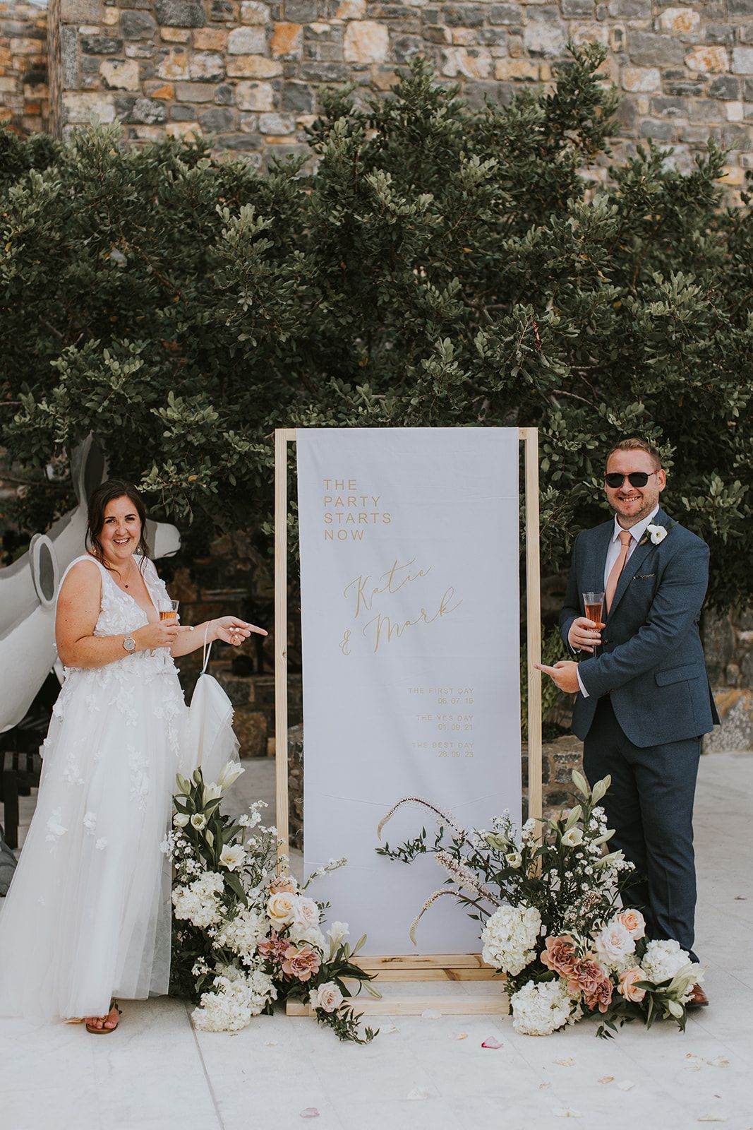 Nina& Samouel - In a beautiful symphony of nature and romance, this scene captures the essence of a perfect coastal celebration. The gentle breeze carries sweet floral whispers as the couple walks amidst a cascade of pastel petals, their smiles reflecting joy and love. The soft blues of the ocean and sky provide a serene backdrop, harmonizing with the lush greenery and delicate whites and pinks of the blooms. This composition encapsulates an idyllic, nature-infused elegance, showcasing the artistry and thoughtful design of the florist's craft. - Photo 5