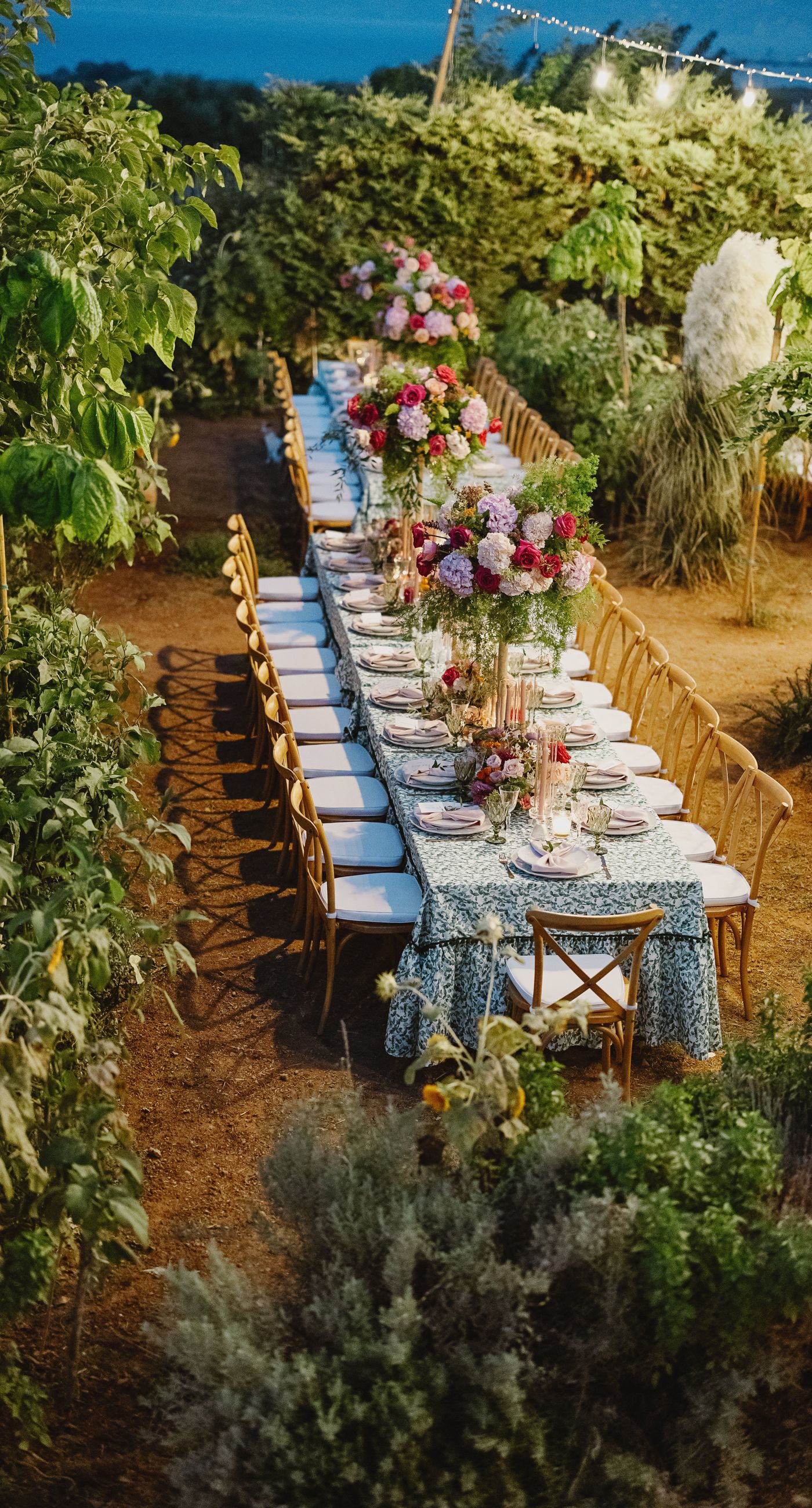 Where Celebration Meets Nature - A modern garden wedding with clean lines and a strong sense of a curated dining experience.
Long communal tables set within the vineyard, statement floral arrangements at varying heights, layers of greenery with bold color accents, and warm lighting that carried the atmosphere from day into night. A setting that felt natural yet intentionally designed  contemporary, vibrant, and effortlessly elegant. - Photo 5