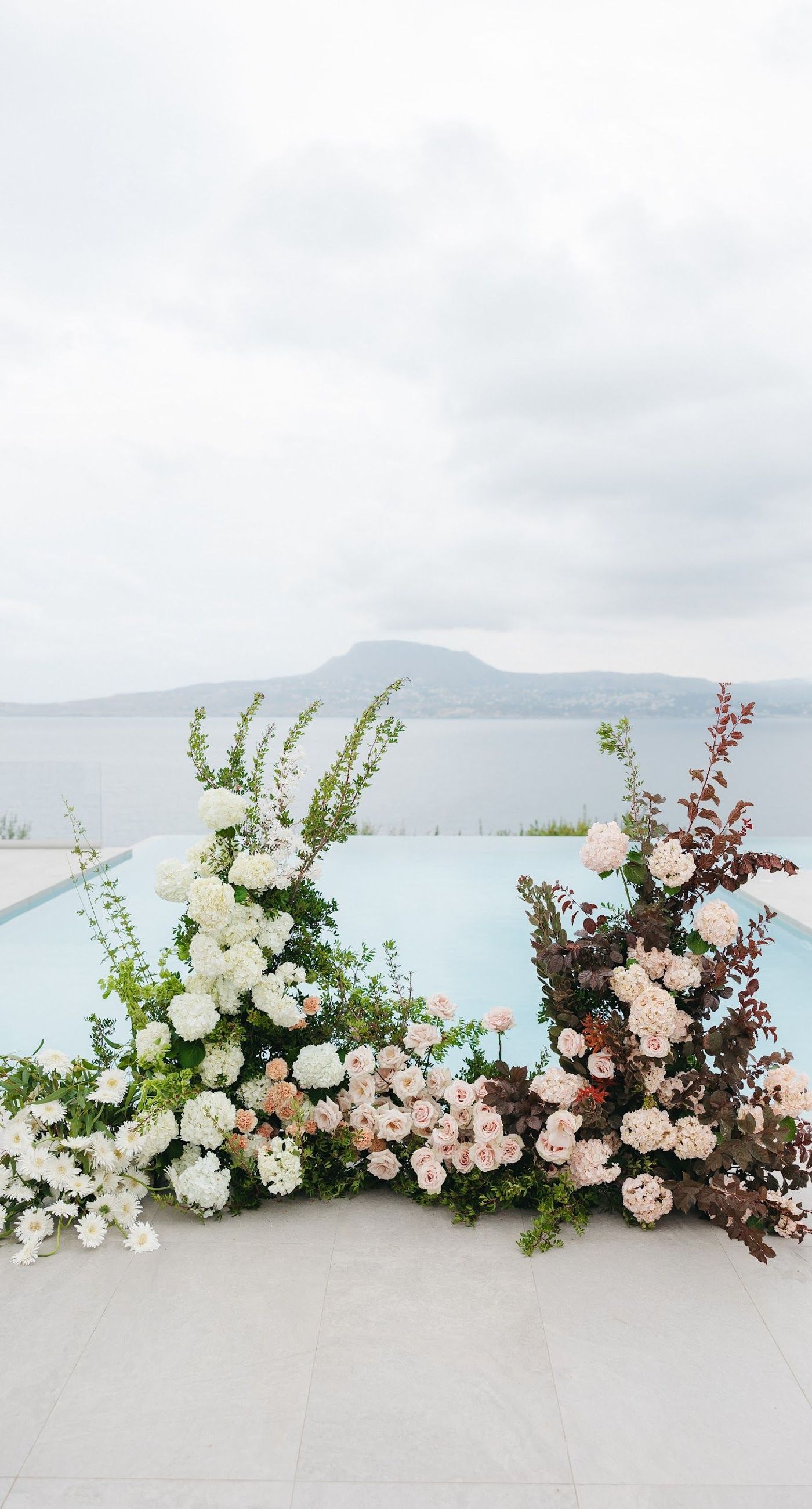 Shay & Vedad - In the serene elegance of a Greek wedding, a mirrored sign stands as a testament to love and artistry. The names "Shay and Vedad" are embossed in sleek white typography, reflecting a moment of intimate celebration bathed in soft, natural light. The minimalist, contemporary aesthetic is accented by subtle greenery, evoking a sense of tranquility and romance amidst the timeless beauty of Crete. The composition captures the harmonious blend of modern elegance with organic details, drawing you into a world where love and nature seamlessly intertwine. - Photo 2