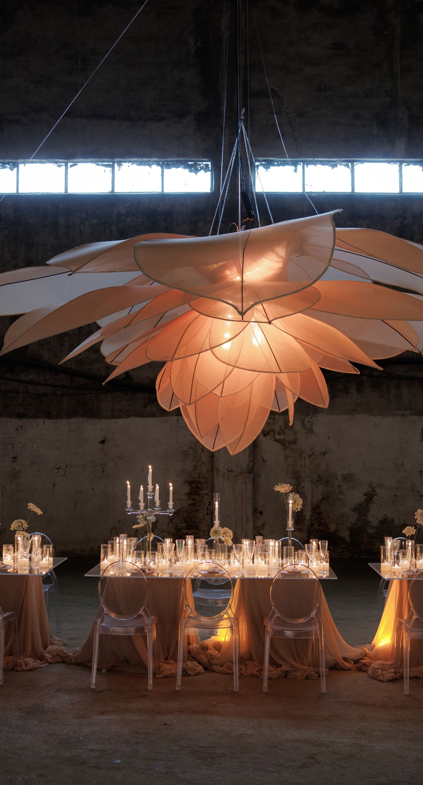 The Extravaganza Flower - Set within an industrial space, this project was conceived as an atmospheric dining experience where light and form take center stage. A sculptural, suspended installation “blooms” above the table, creating depth and scenography, while a candlelit setup adds warmth and intimacy. Clean lines, transparent materials, and subtle florals complete a design that goes beyond decoration it is installation art with emotion. - Photo 5